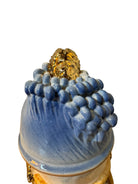 Handcrafted ceramic sculpture in the shape of a foot, decorated with intricate black and white patterns, 24KT gold accents, and topped with a blue lid featuring a gilt fish and head emerging from stylized waves.