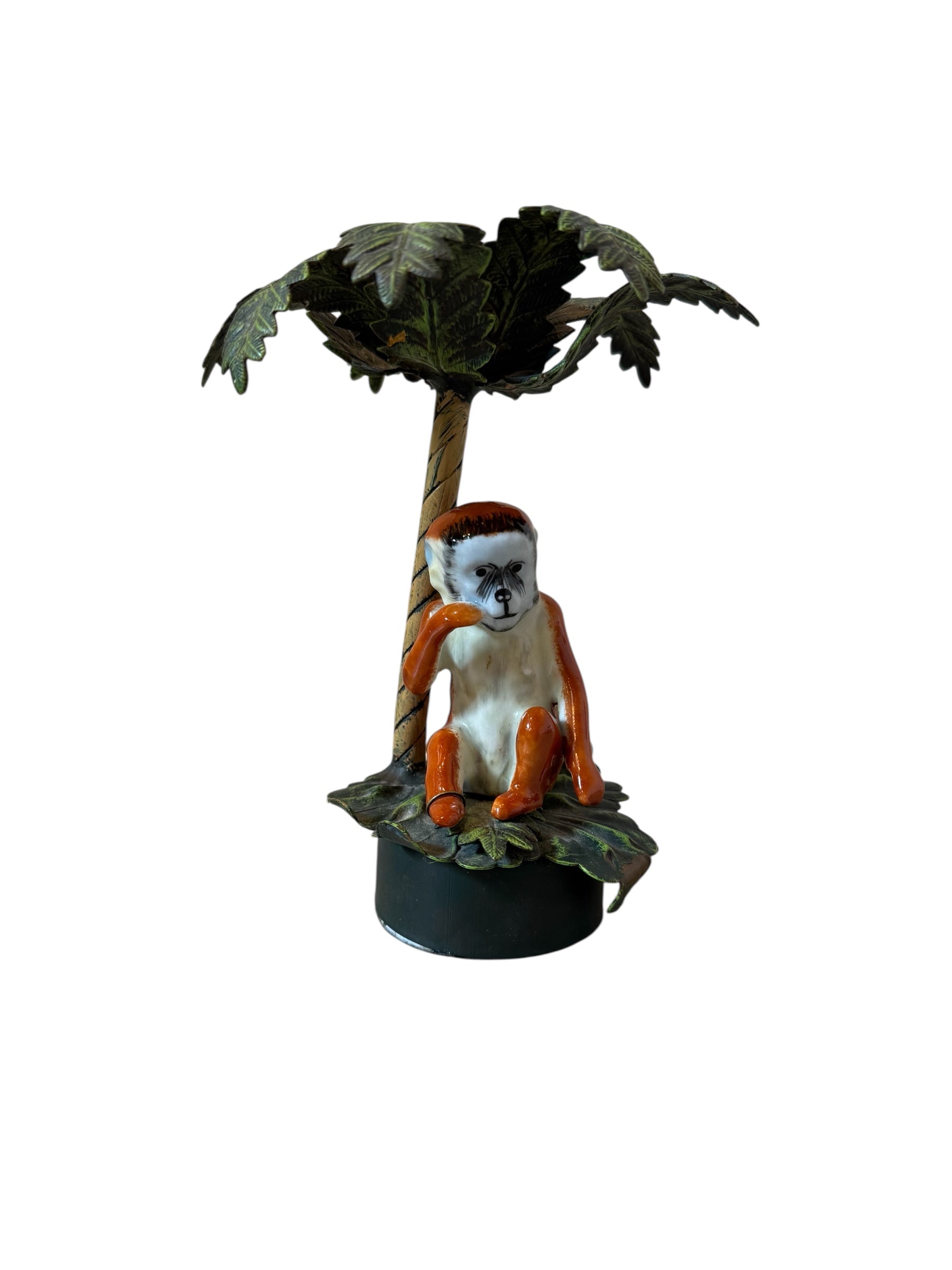 Small monkey figurine sitting on a branch with a palm tree against a white background