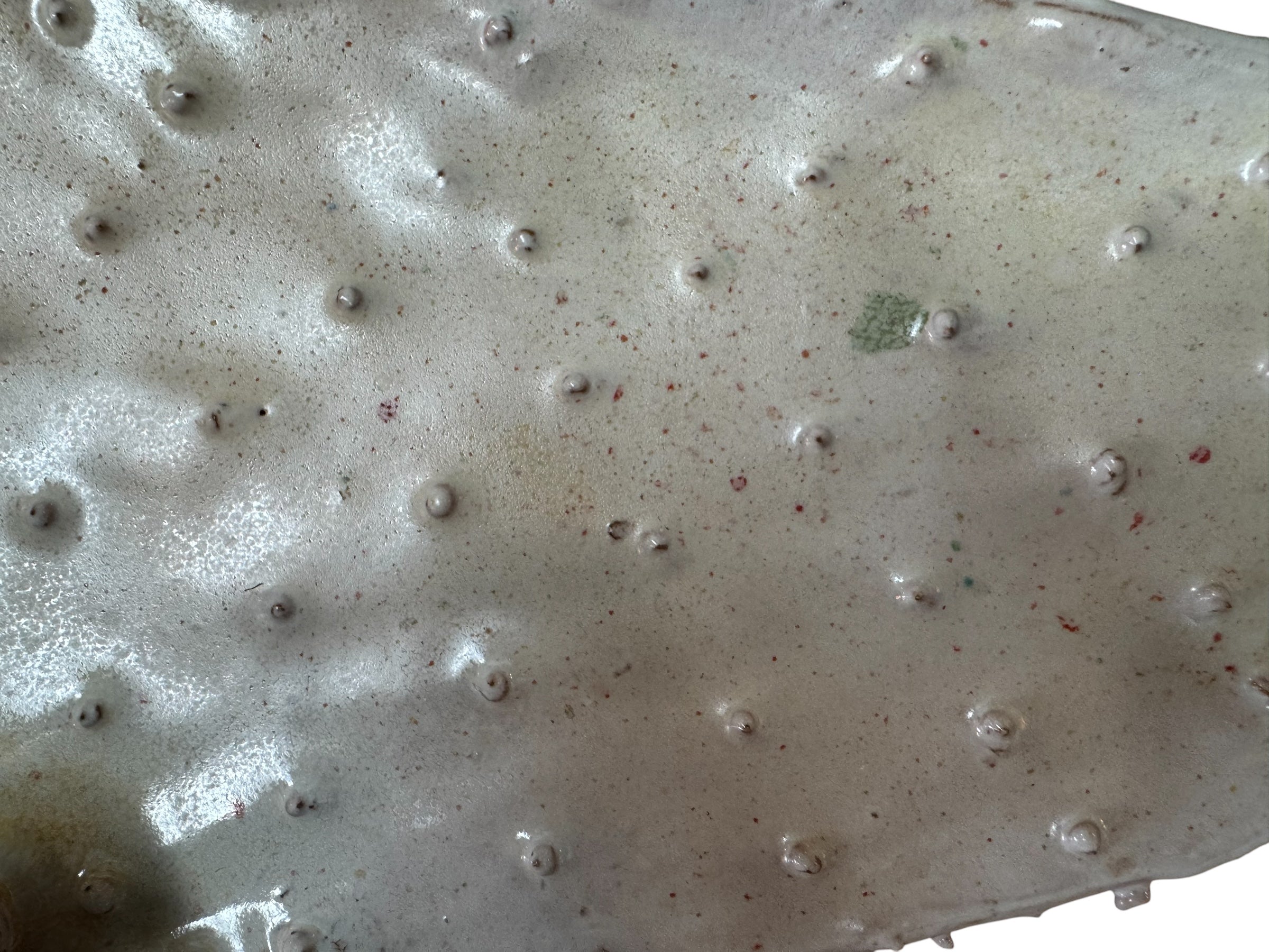 A white and orange, glazed ceramic platter in the shape of a prickly pear cactus pad with attached prickly pear fruit. The surface has raised dots representing spines.