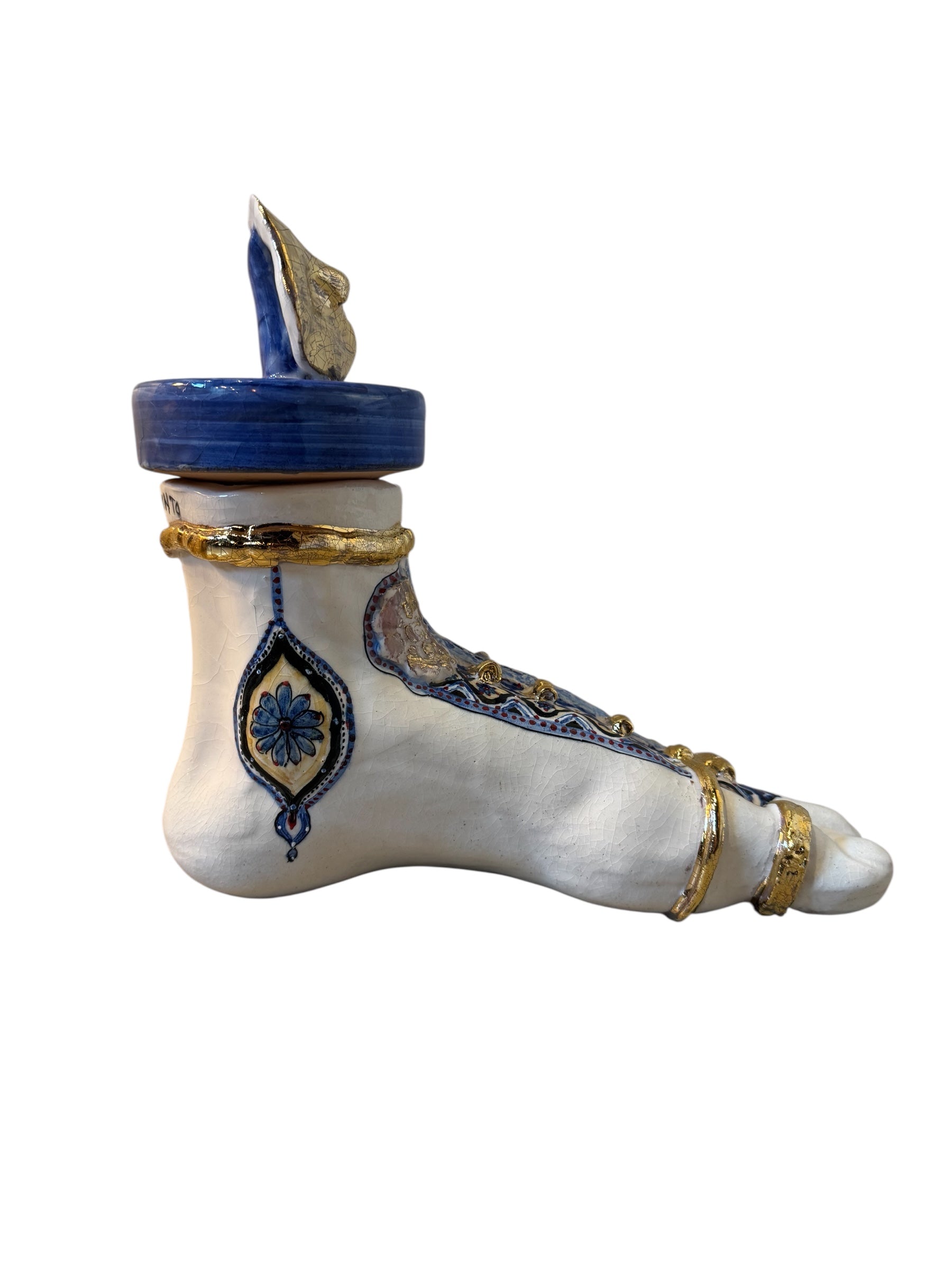 Close-up of a ceramic foot sculpture by Domenico Pinto. The foot is decorated with intricate hand-painted designs inspired by Apulian folklore and accented with 24KT gold. A stylized gilt mask sits atop the foot.