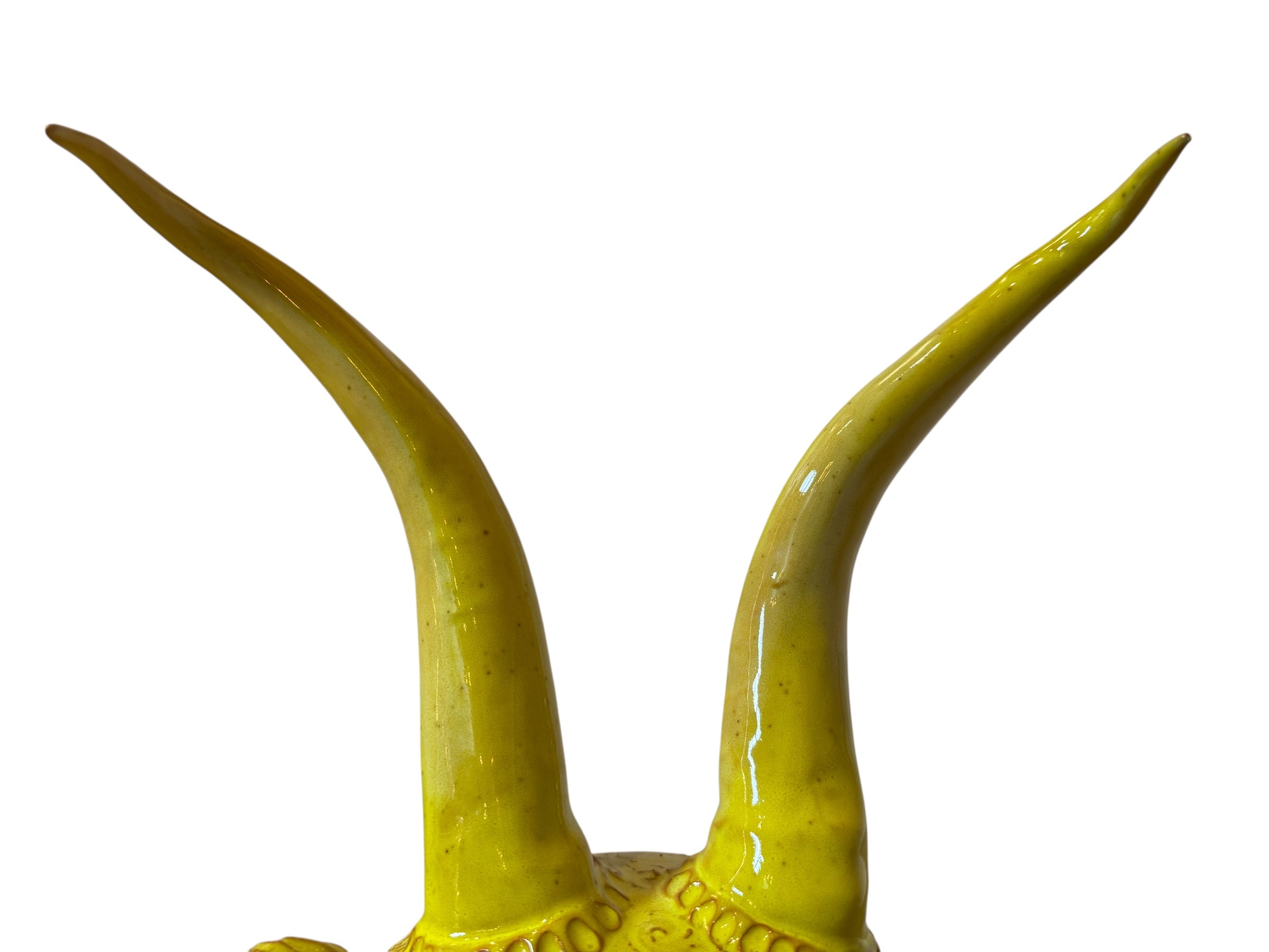 Yellow ceramic sculpture titled 'The Ram Oracle' by Enza Fasano, featuring a round body with intricate, hand-incised patterns and long, stylized ram-like horns