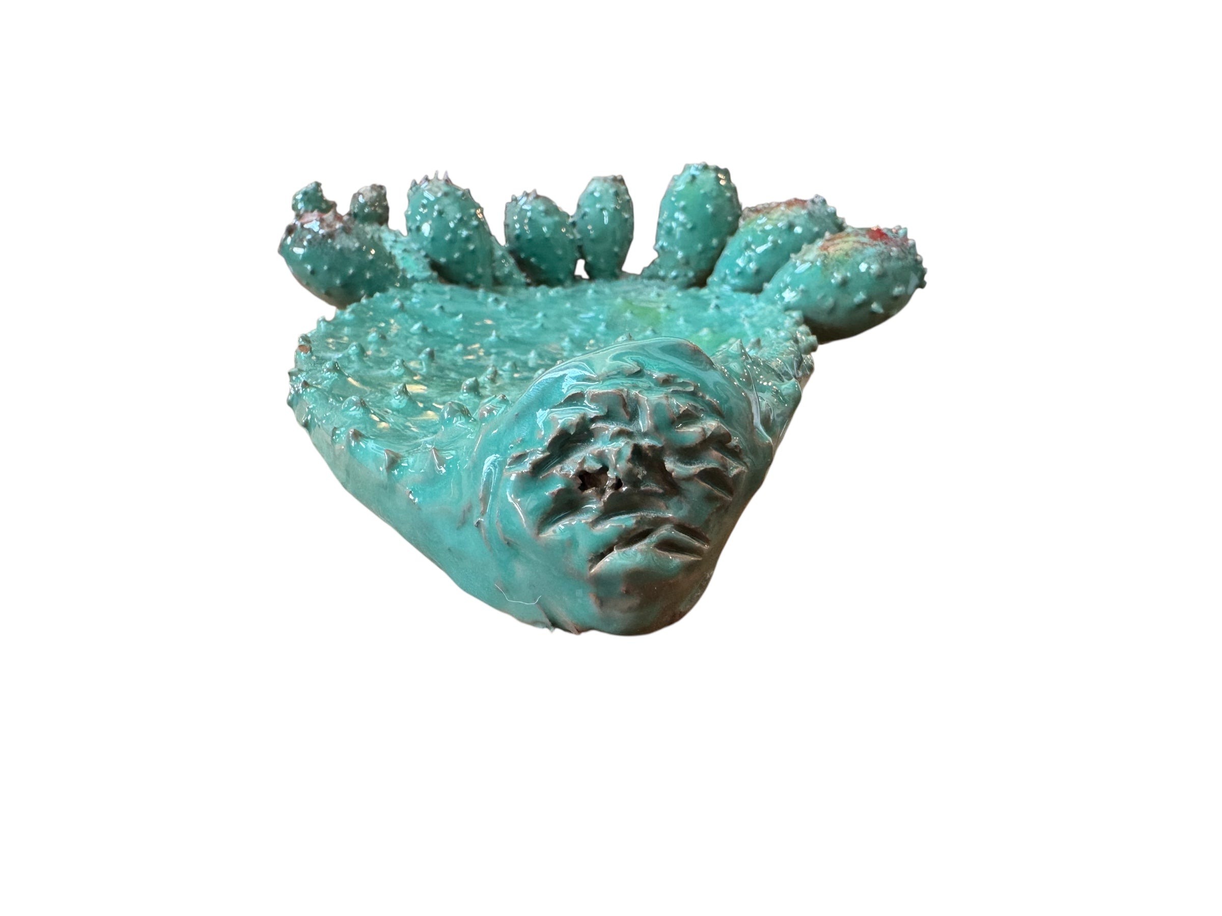A green and red, glazed ceramic platter in the shape of a prickly pear cactus pad with attached prickly pear fruit. The surface has raised dots representing spines.