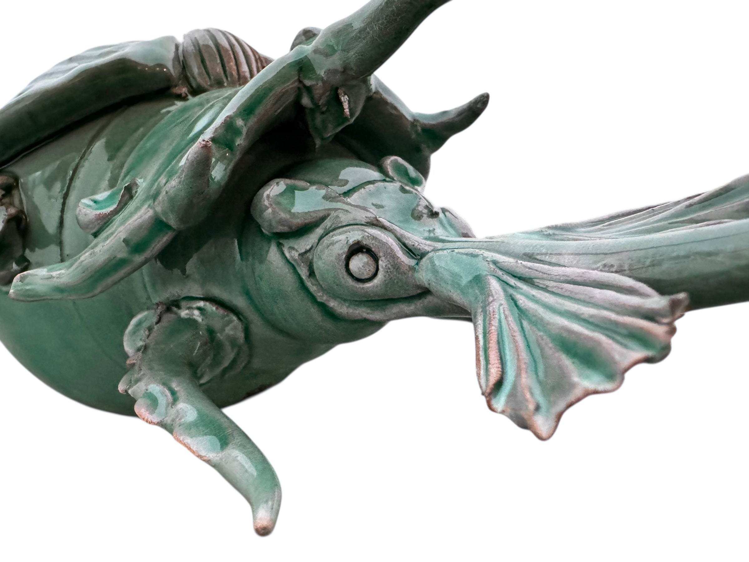 A ceramic sculpture of a stylized beetle by Enza Fasano, featuring a deep emerald green glaze with dark, metallic bronze-colored accents. The beetle is depicted with a highly textured, ribbed shell (elytra) and prominent, curved horns. Its legs are stylized with suckers, reminiscent of octopus tentacles. The piece has a glossy finish and rests against a plain white background.