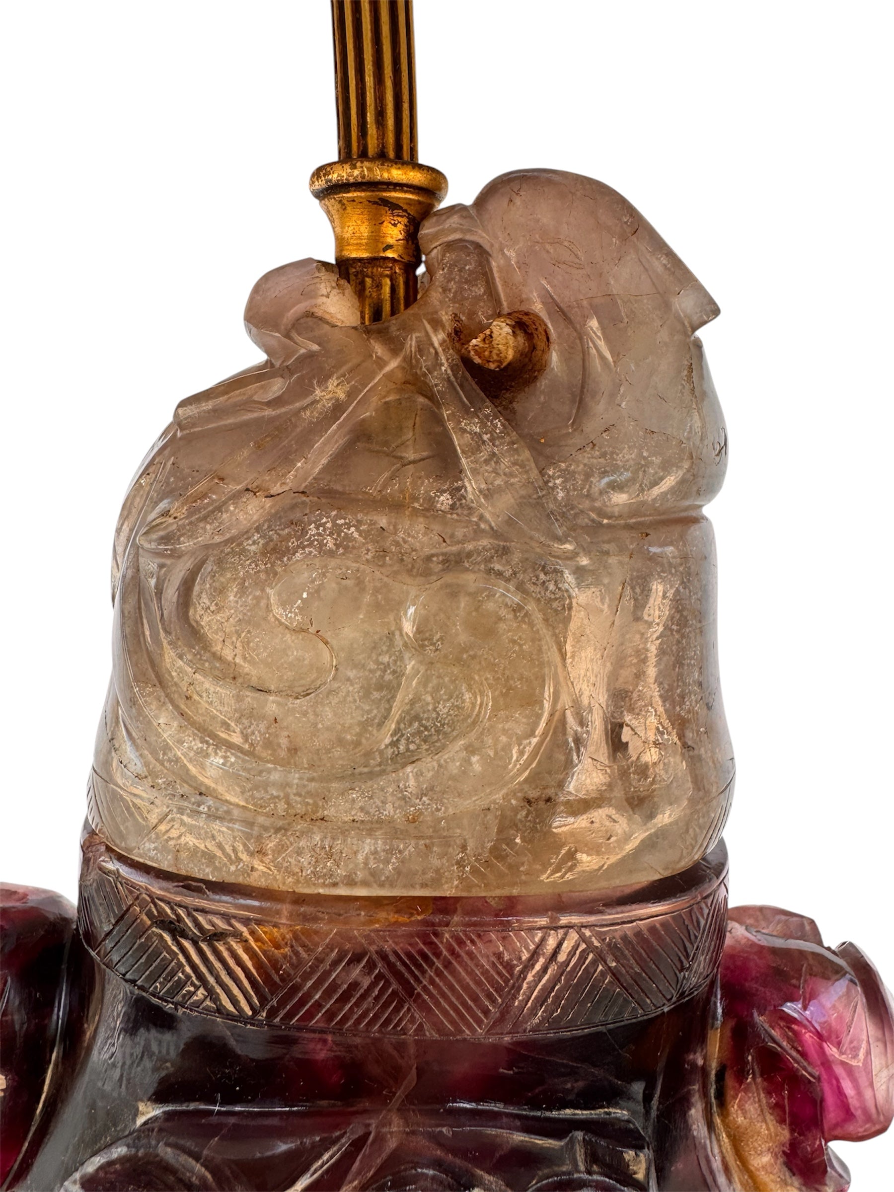 An antique Chinese table lamp featuring a base hand-carved from deep purple amethyst stone, topped with a clear quartz crystal neck. The lamp sits on an ornate, custom gilt-bronze Chinoiserie base and features a flared, cream-colored silk lampshade still enclosed in protective plastic. A rectangular brass finial sits at the very top.