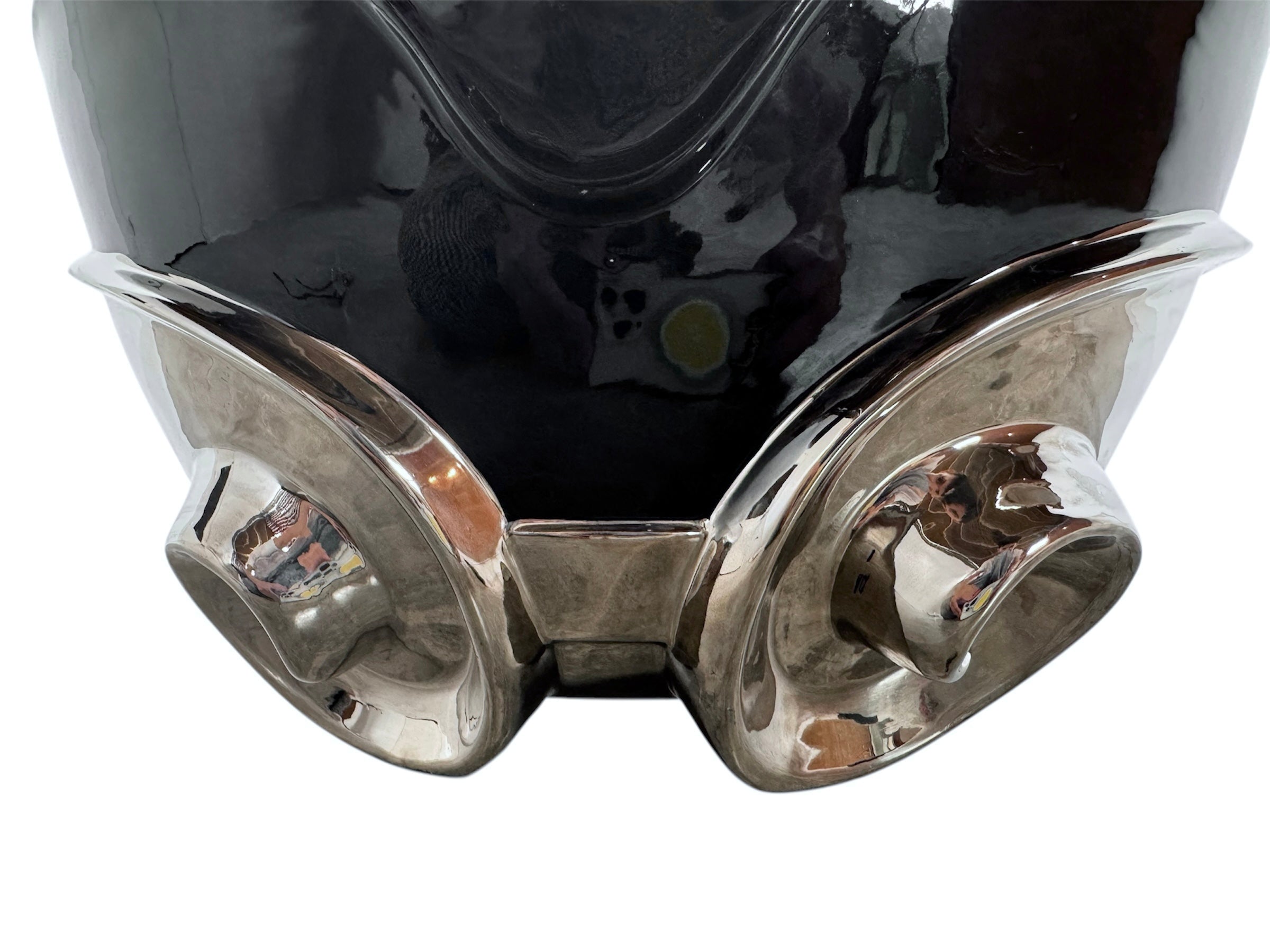 A large, decorative ceramic bowl by Dolbi Cashier in a dramatic Postmodern style. The top half is finished in a polished, piano-black glaze with an organic, wavy "butterfly" rim that dips in the center and rises at the sides. The bottom half is finished in a reflective, metallic silver chrome glaze, featuring bold, geometric-rounded feet and a structured base that appears to "hold" the black vessel. The overall shape is wide and sculptural, reminiscent of 1980s Art Deco Revival.