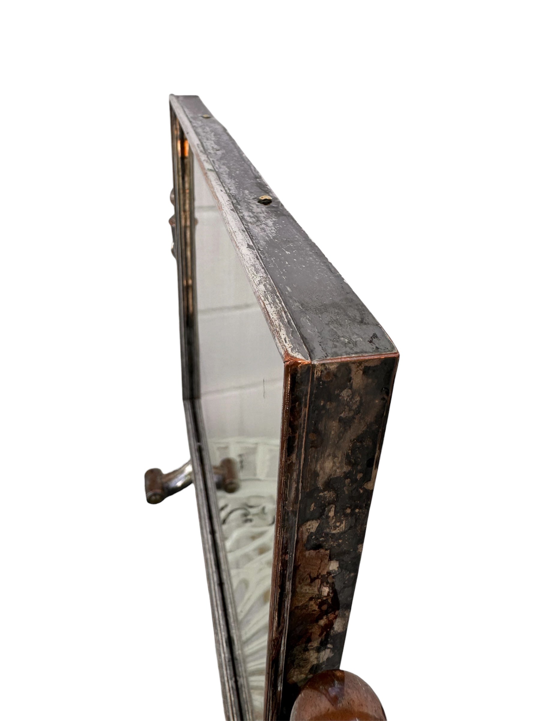The antique Chevalier Mirror features a rectangular swing frame supported by two turned posts on decorative trestle feet. The mirror stands on four scrolled feet and features its original tarnished, silvered finish. The front of the mirror reflects a bright blue sky with wispy white clouds. The original dark brown backing is still attached to the frame.