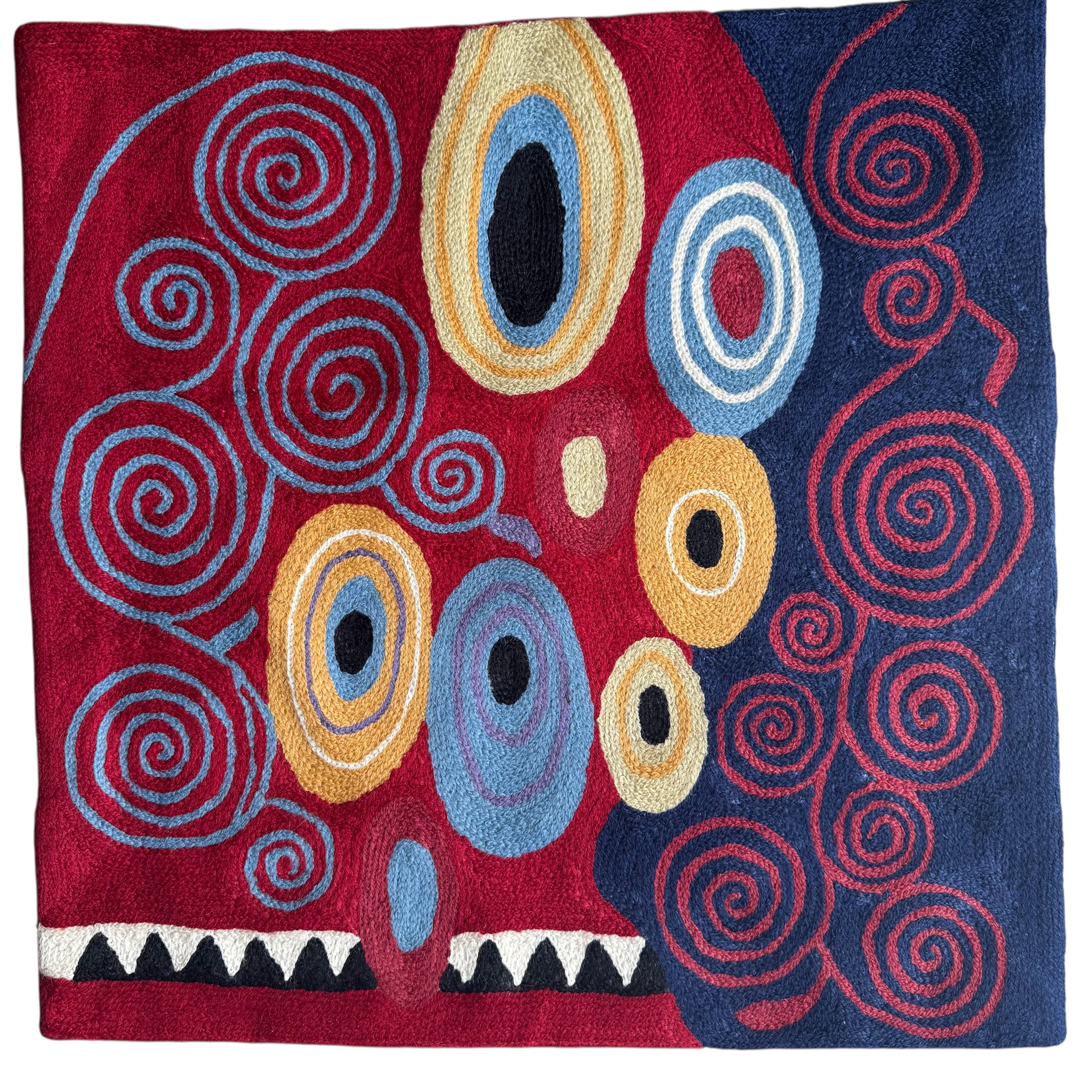 Colorful abstract design rug with circular patterns on a red, blue, and yellow background. Vibrant cross-stitched pillows from India with various artistic designs, sourced in Aix-en-Provence.