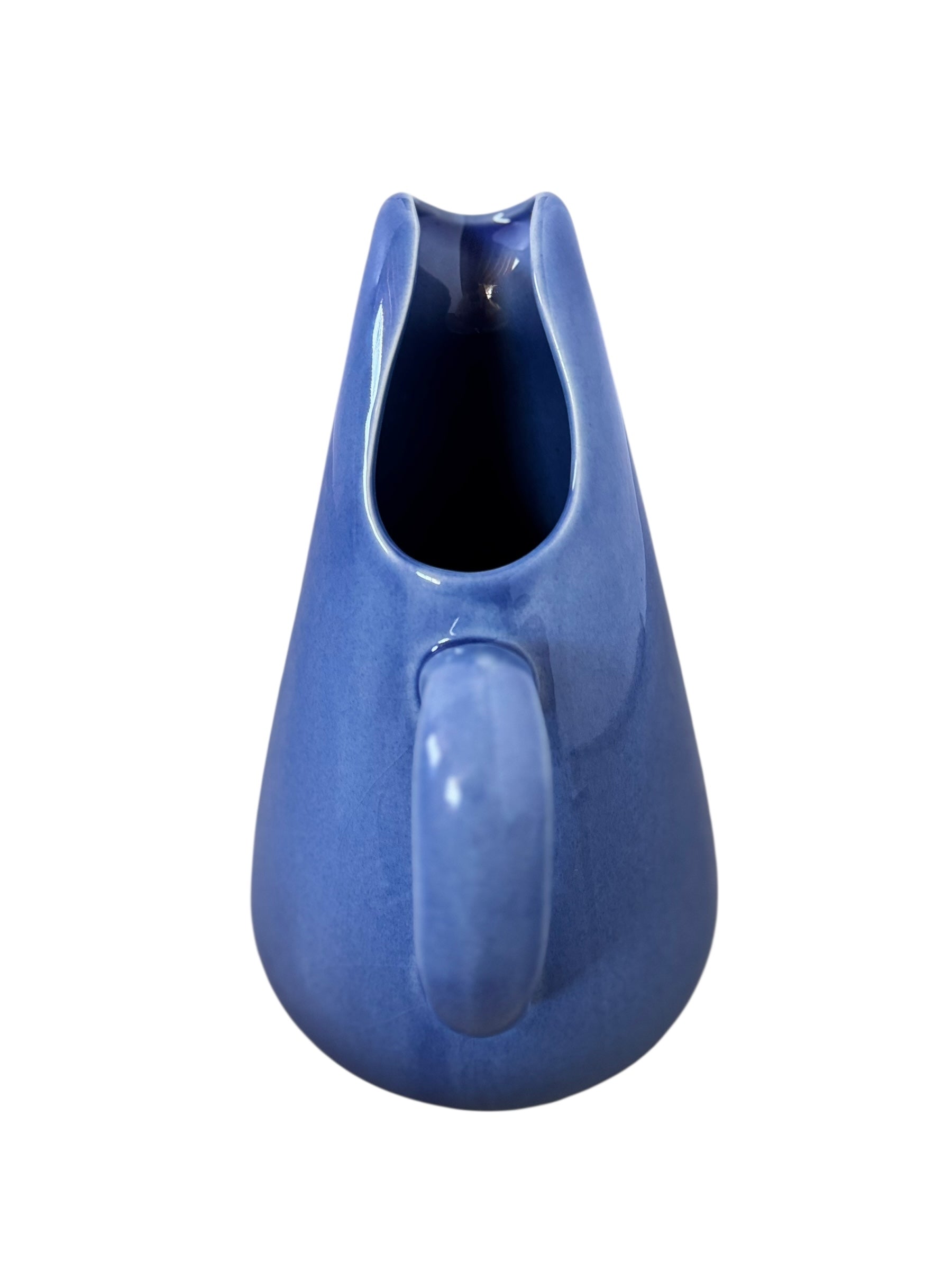 A Russel Wright American Modern stoneware water pitcher in a glossy Manitoga blue glaze is centered against a white background. The pitcher has a teardrop shape, a large handle, and a wide spout