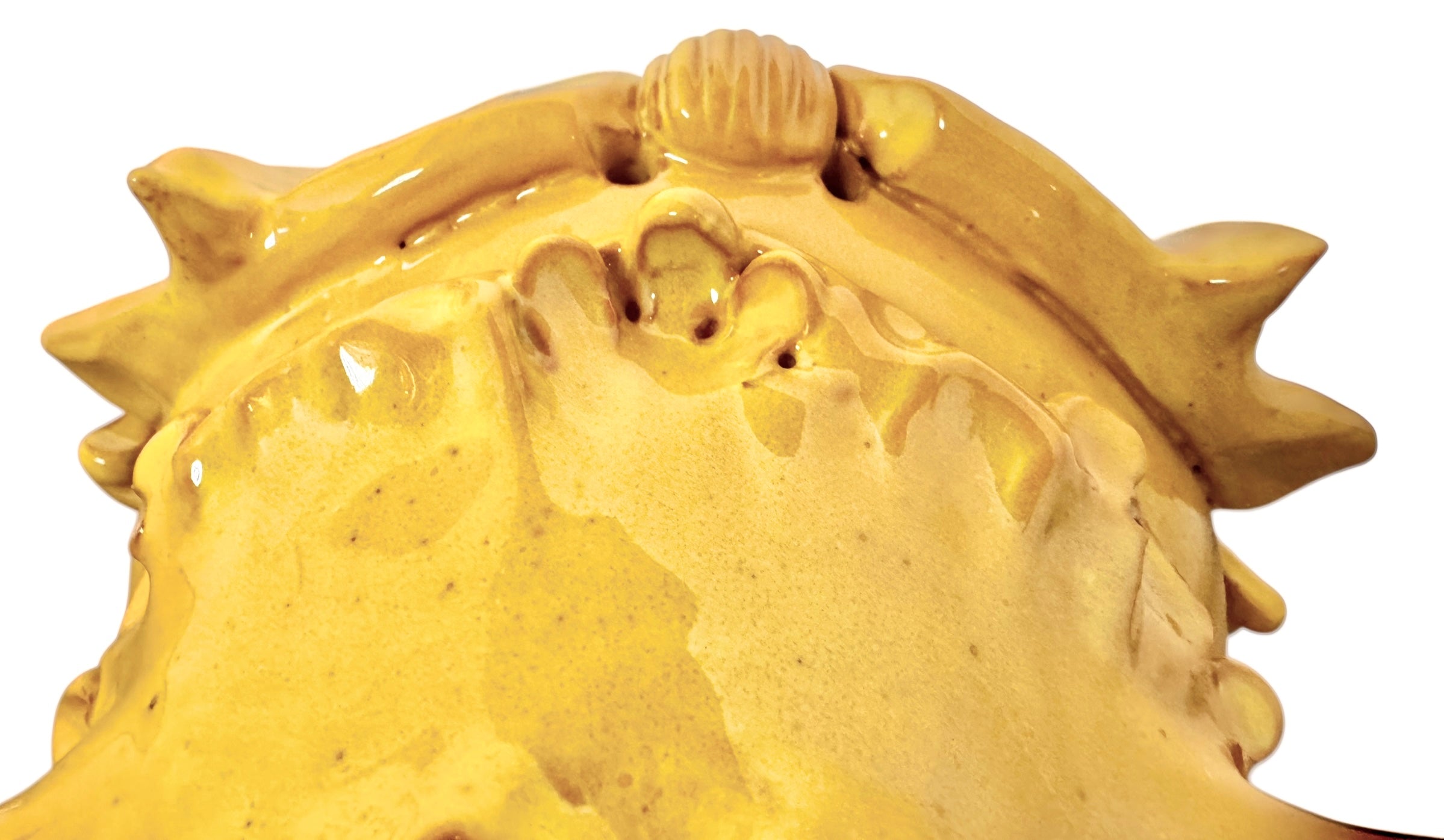 a large, high-gloss ceramic sculpture by Enza Fasano, shaped like a stylized beetle. The entire piece is finished in a warm, honey-yellow glaze. The beetle features prominent, curved mandibles at the front, a textured "collar" area, and a rounded, shell-like body with decorative ridges along the edges. The surface is smooth and reflective, catching the light across its organic contours.