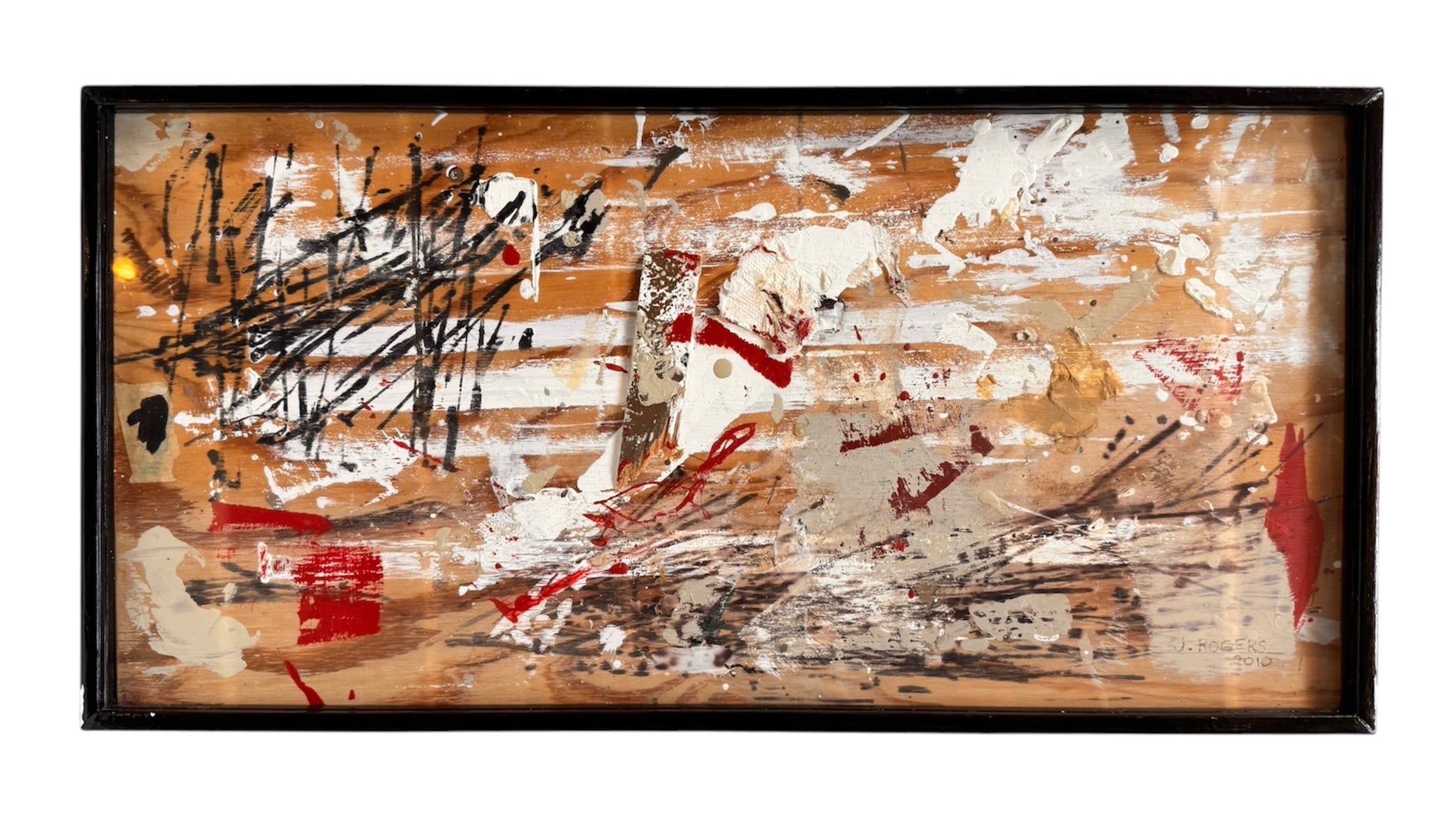 horizontal rectangular mixed media abstract artwork by J. Rogers, dated 2010, presented in a thin black frame. The composition is set against a light-toned wood grain background and features a dynamic, gestural arrangement of thick white impasto, splatters of red and black paint, and aggressive black scribbles. A vertical strip of textured material is collaged near the center, while various washes of tan and cream create a sense of weathered depth across the wooden surface.