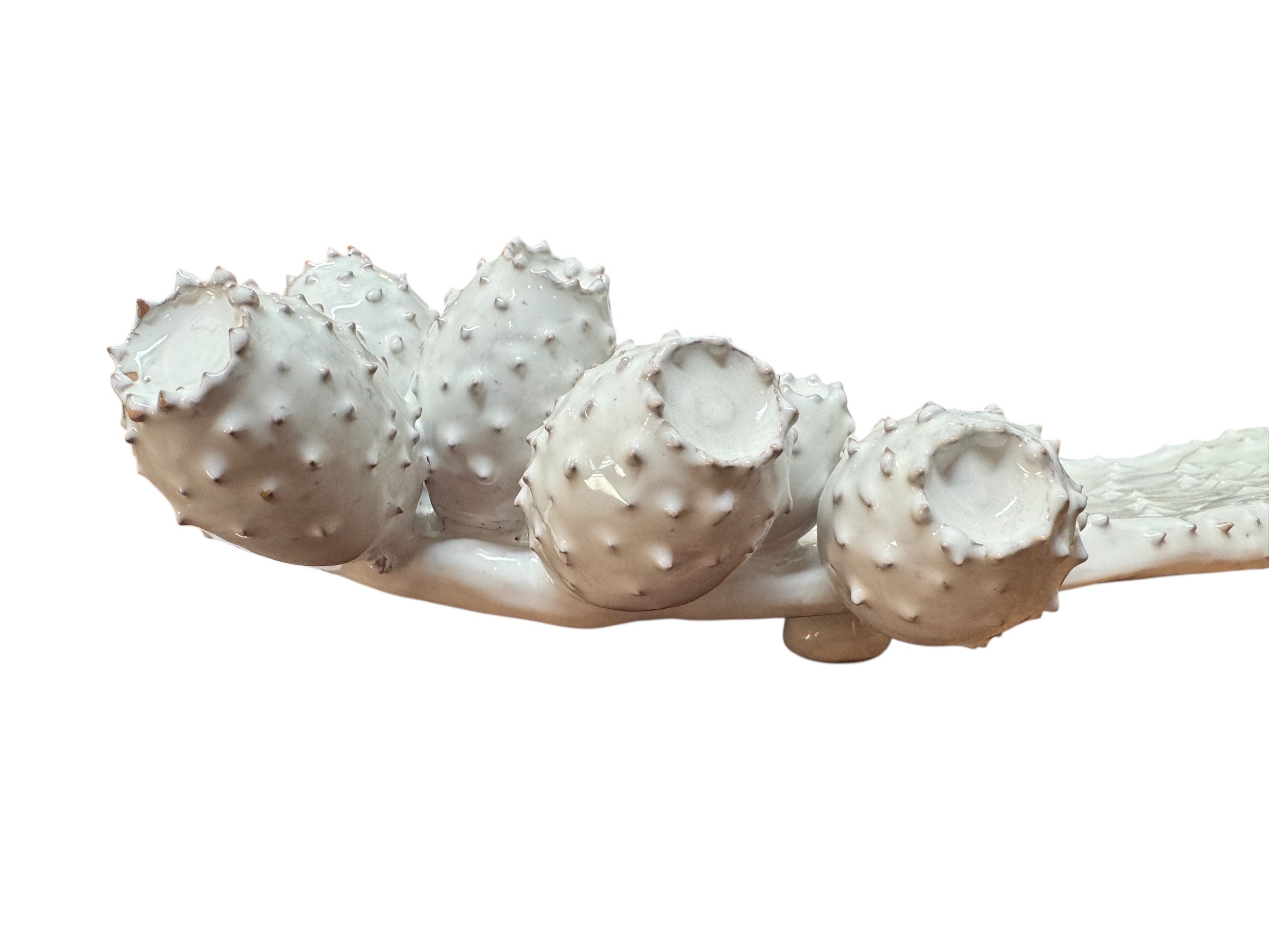 A white, glazed ceramic platter in the shape of a prickly pear cactus pad with attached prickly pear fruit. The surface has raised dots representing spines.