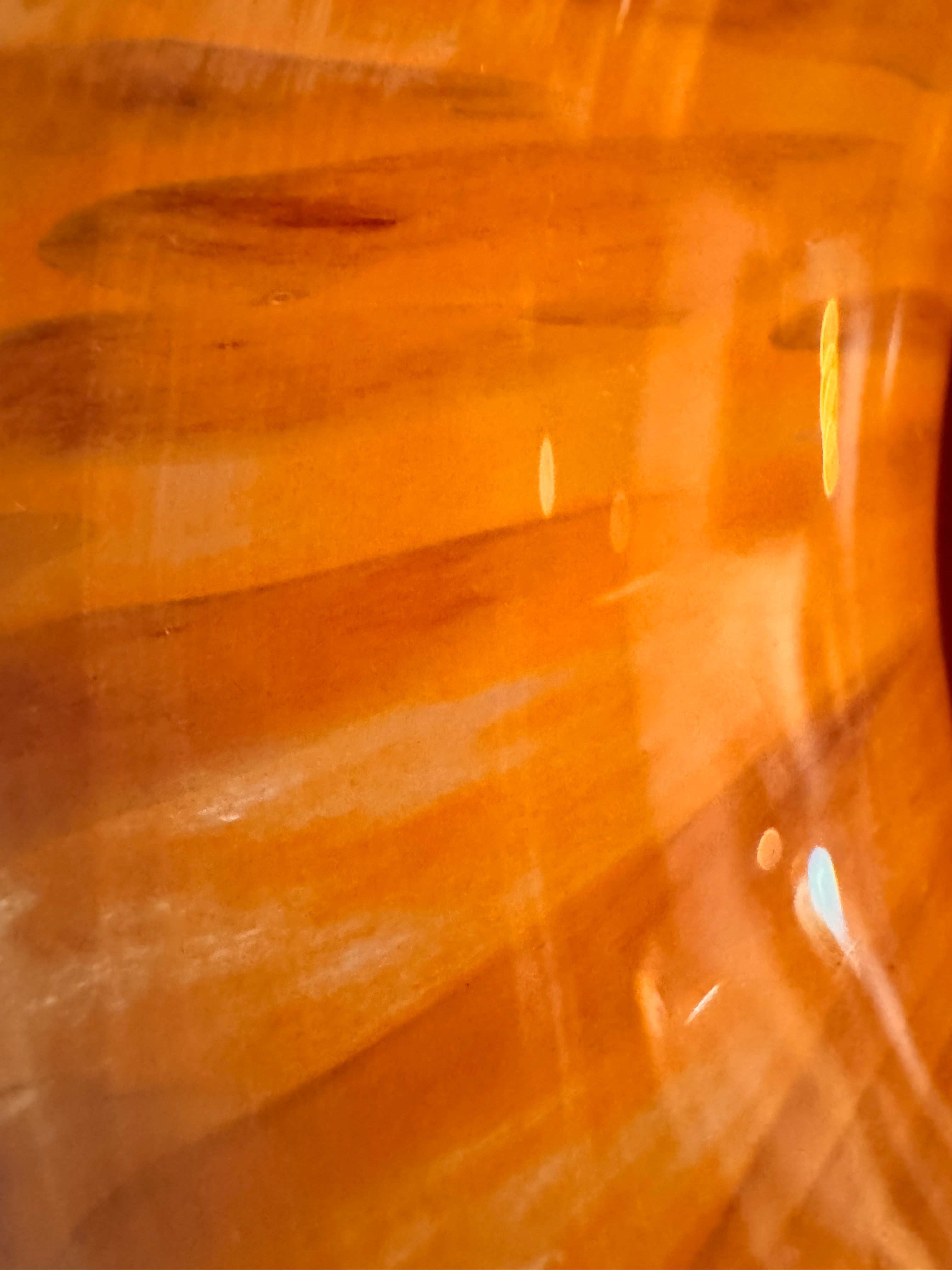 A hand-blown Italian Murano glass vase featuring a wide, bulbous body and a short, flared rim. The glass is a vibrant, translucent amber-orange base decorated with an organic "macchia" or spotted pattern of deep ruby red blotches. The red spots are elongated and vertical near the neck, becoming larger and more rounded toward the base. The surface has a high-gloss, reflective finish, showcasing mid-century modern craftsmanship.