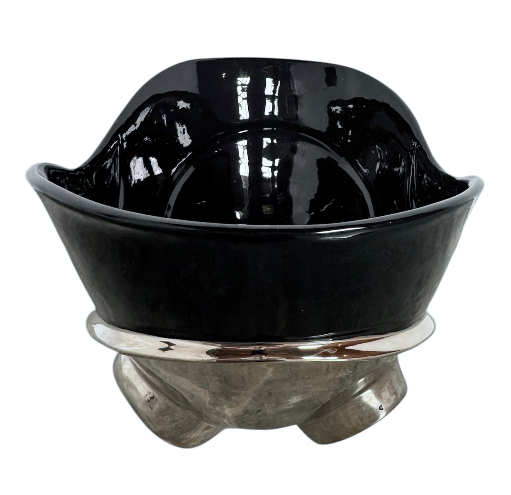 A large, decorative ceramic bowl by Dolbi Cashier in a dramatic Postmodern style. The top half is finished in a polished, piano-black glaze with an organic, wavy "butterfly" rim that dips in the center and rises at the sides. The bottom half is finished in a reflective, metallic silver chrome glaze, featuring bold, geometric-rounded feet and a structured base that appears to "hold" the black vessel. The overall shape is wide and sculptural, reminiscent of 1980s Art Deco Revival.