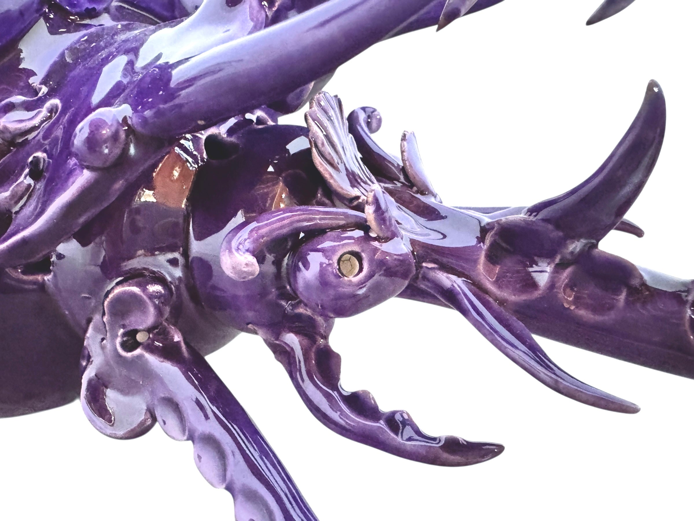 A glossy, deep purple ceramic sculpture of a beetle by Enza Fasano. The piece features a highly stylized and ornate design, blending insect-like anatomy with fantastical elements. It has a smooth, rounded shell and elongated, curved mandibles and appendages lined with sharp, thorn-like protrusions. The monochromatic glaze is reflective, highlighting the intricate sculptural details and textures of the avant-garde artwork.