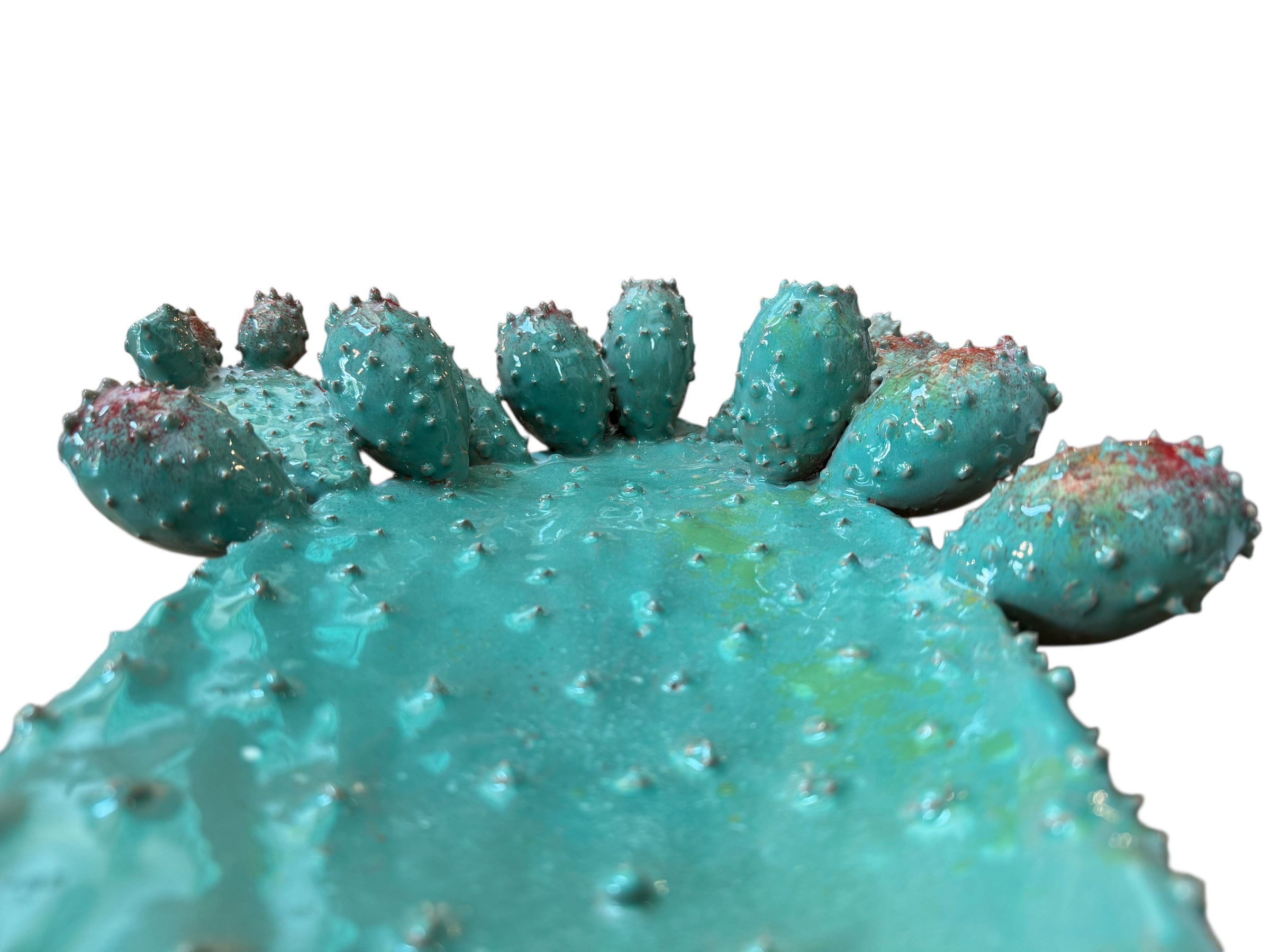A green and red, glazed ceramic platter in the shape of a prickly pear cactus pad with attached prickly pear fruit. The surface has raised dots representing spines.