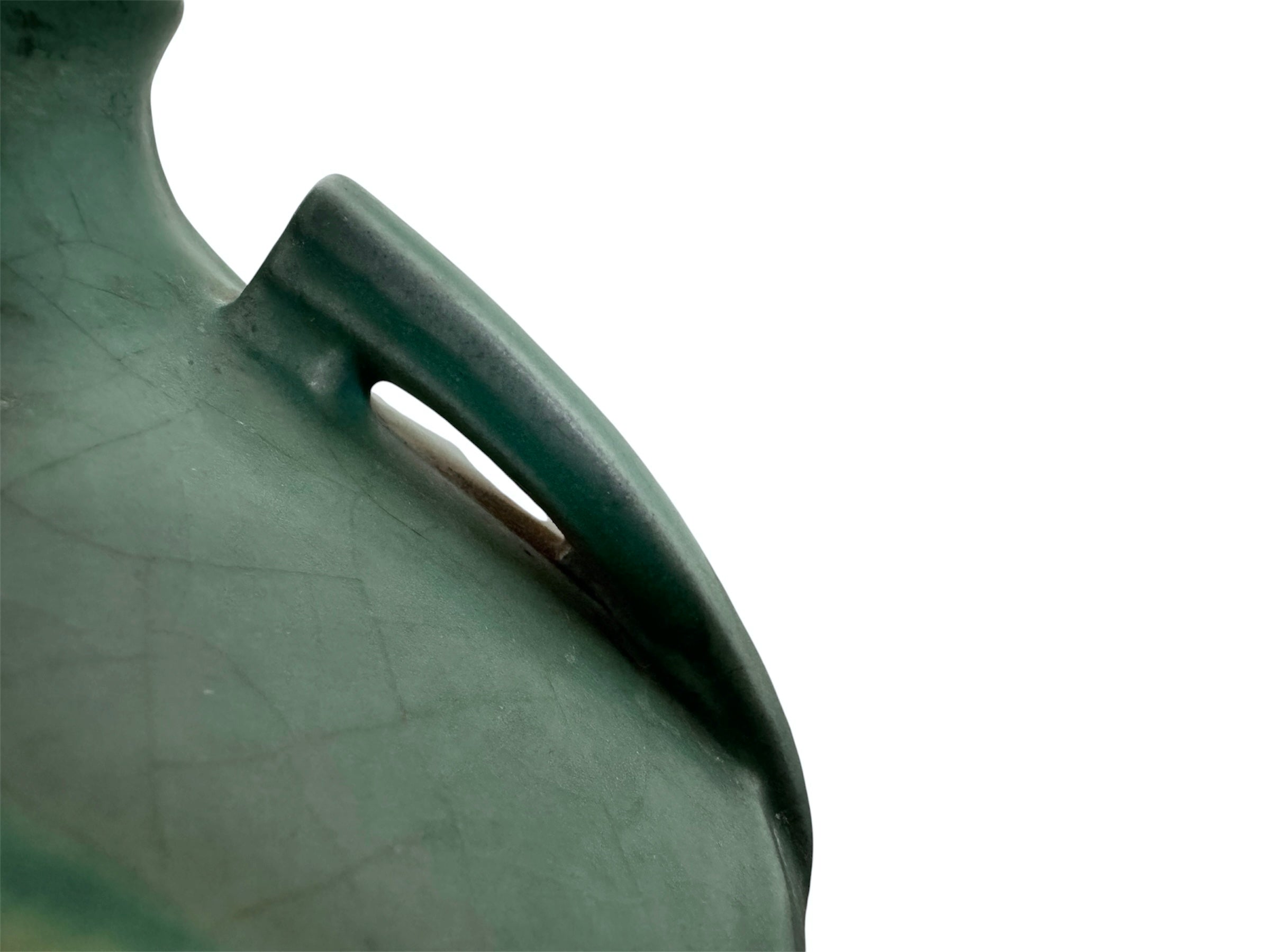 A squat, rounded vintage Roseville pottery vase in a light teal-blue matte glaze. The vase features two small, angular geometric handles on its shoulders and a flared rim. Embossed on the front is a cluster of textured, green and pale-yellow thornapple blossoms tucked against sharp, serrated green leaves. The surface shows a subtle, fine network of age-related crazing lines throughout the glaze.