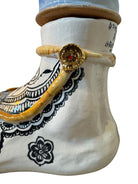 Handcrafted ceramic sculpture in the shape of a foot, decorated with intricate black and white patterns, 24KT gold accents, and topped with a blue lid featuring a gilt fish and head emerging from stylized waves.