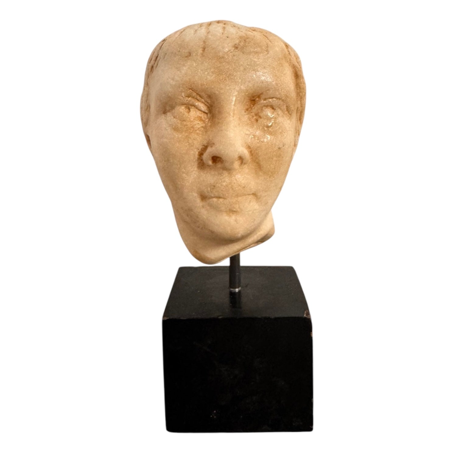 An ancient marble sculpted head of a young man, presented on a modern black presentation stand. The sculpture is rendered in a three-quarter view, angled slightly to the right, showing a classical profile characterized by a strong nose, softly contoured cheekbones, and slightly parted lips that convey a quiet, contemplative expression. The hair is carved in short, stylized strands that frame the forehead and ears, characteristic of ancient Roman or Greek portraiture styles.