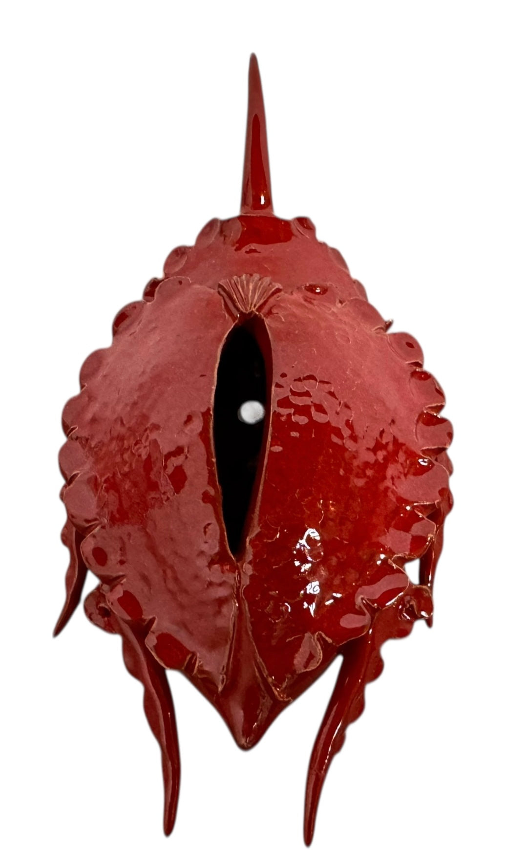 A handcrafted ceramic sculpture of a rhinoceros beetle by Enza Fasano, featuring a vibrant, glossy deep-red glaze. The piece is stylized with smooth, rounded contours and prominent, elegant horns extending forward. Its surface reflects light, highlighting the rich texture and artisanal detail of the clay.