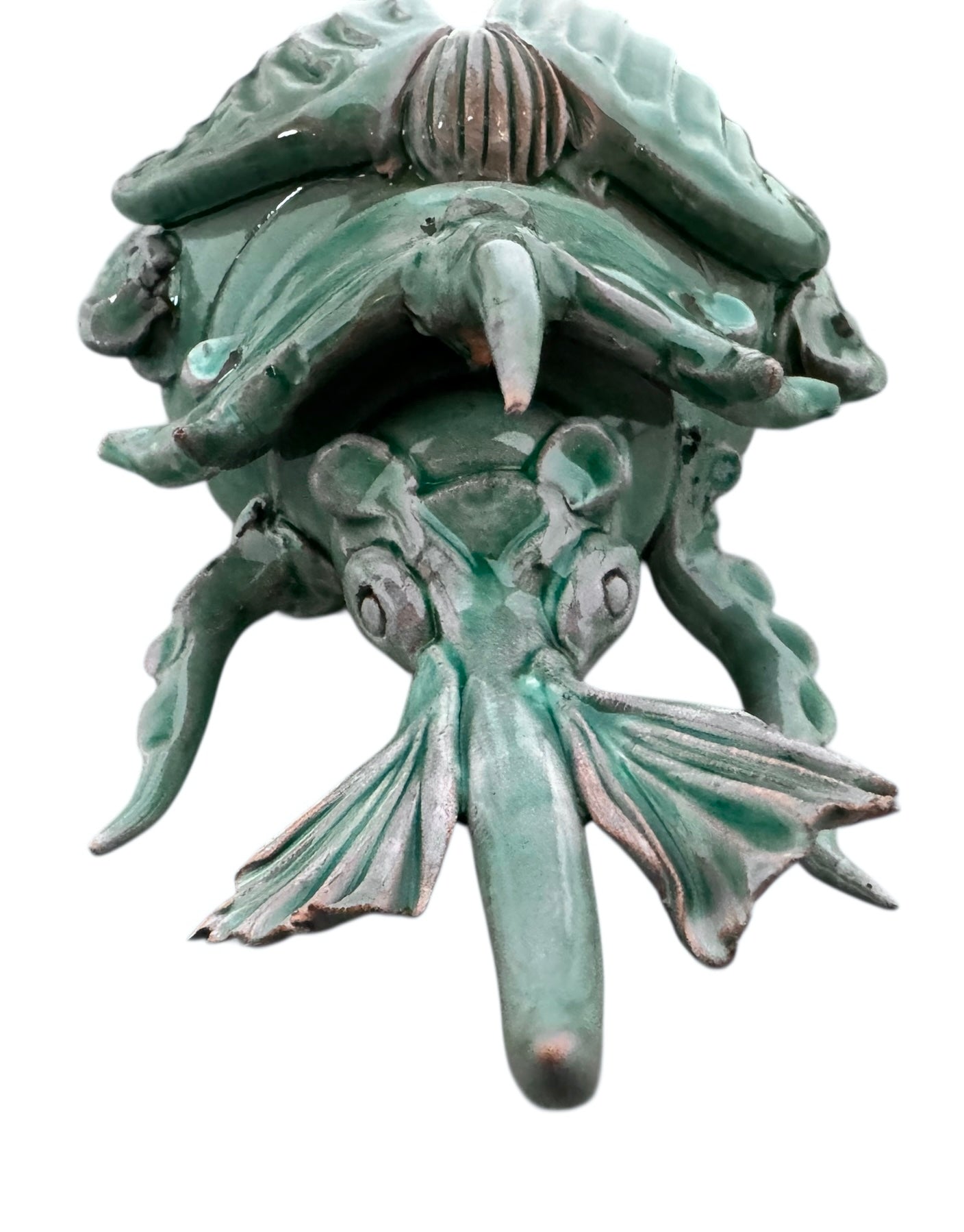 A ceramic sculpture of a stylized beetle by Enza Fasano, featuring a deep emerald green glaze with dark, metallic bronze-colored accents. The beetle is depicted with a highly textured, ribbed shell (elytra) and prominent, curved horns. Its legs are stylized with suckers, reminiscent of octopus tentacles. The piece has a glossy finish and rests against a plain white background.
