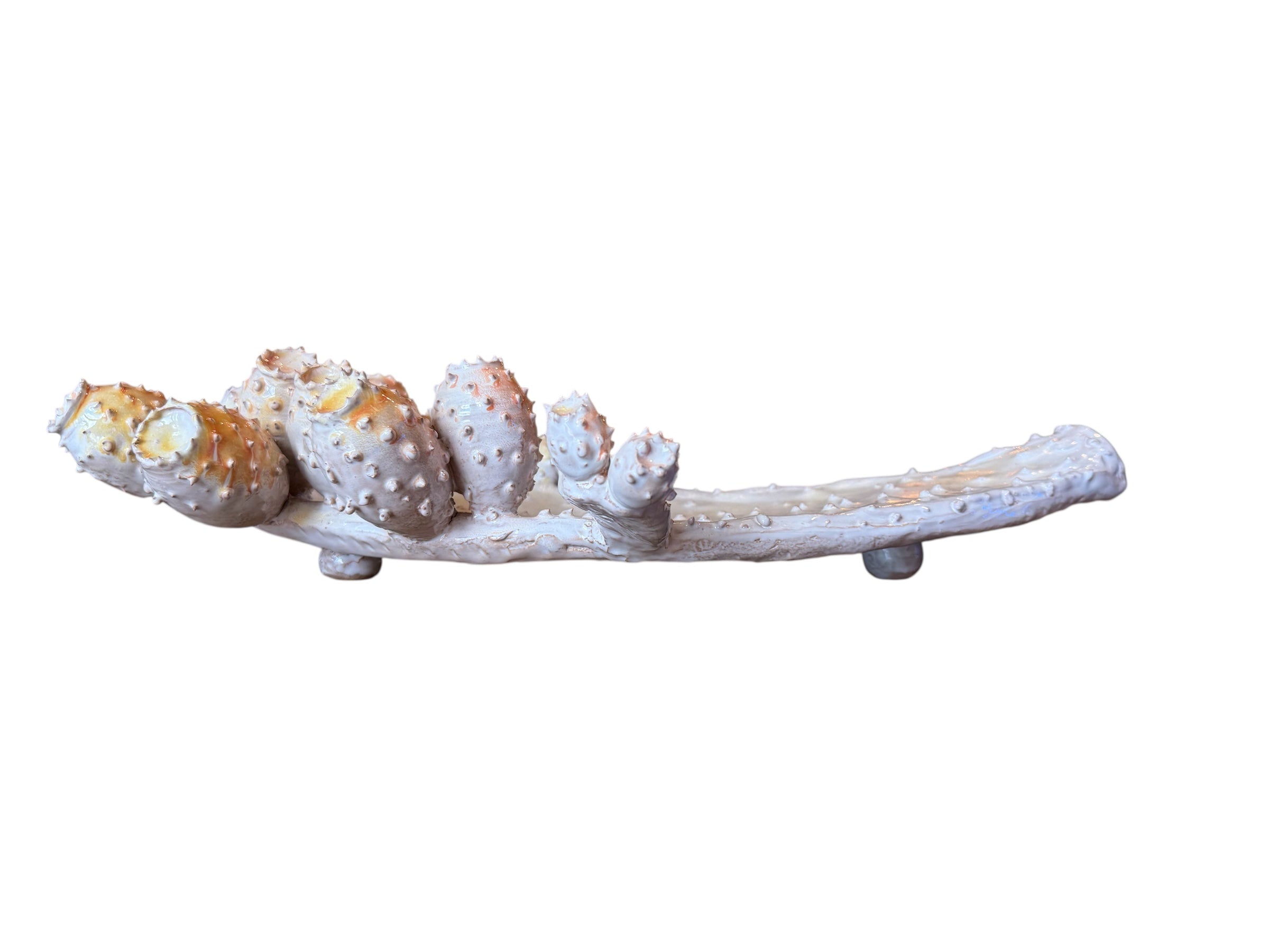 A white and orange, glazed ceramic platter in the shape of a prickly pear cactus pad with attached prickly pear fruit. The surface has raised dots representing spines.