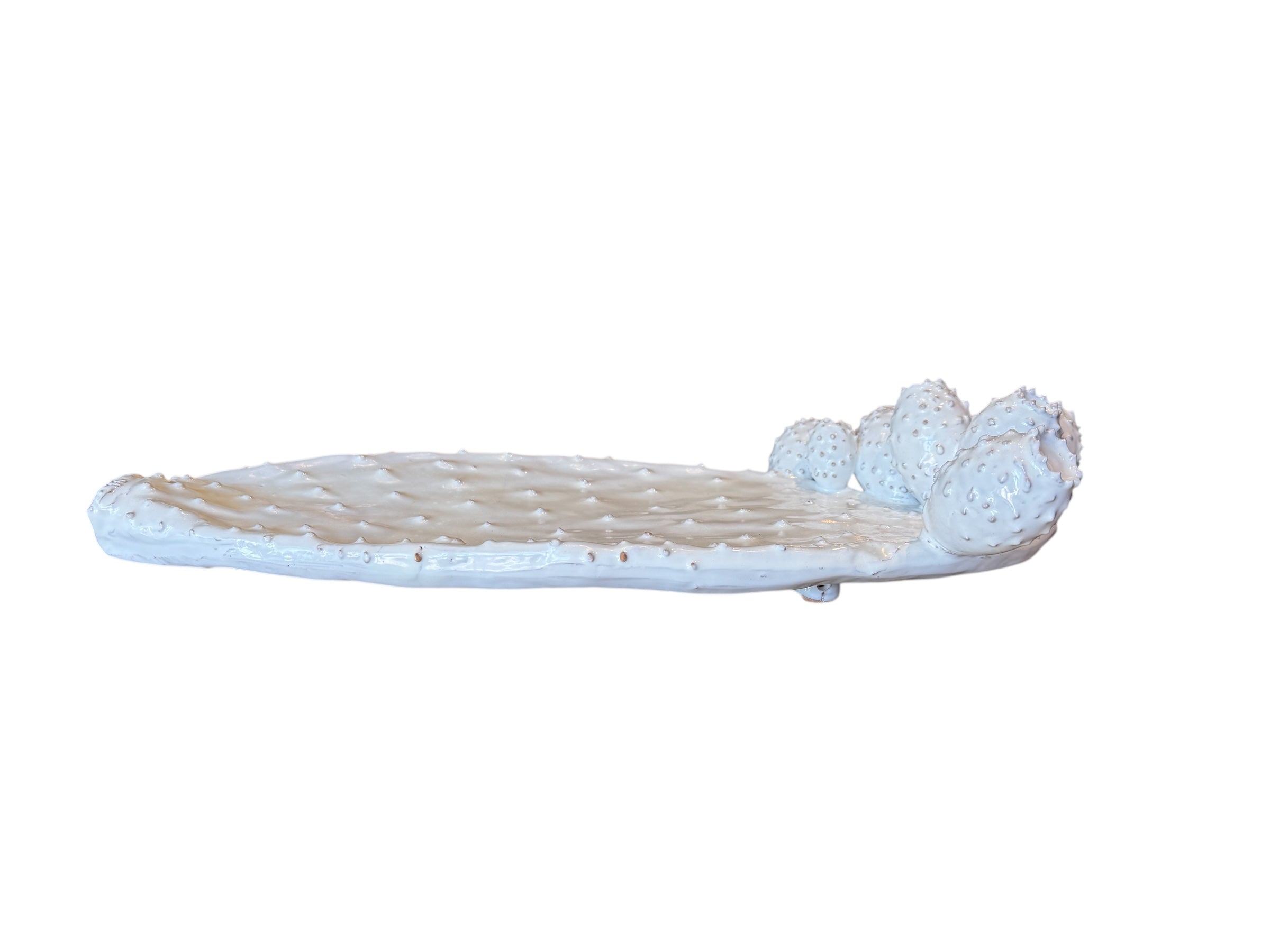 A white, glazed ceramic platter in the shape of a prickly pear cactus pad with attached prickly pear fruit. The surface has raised dots representing spines.
