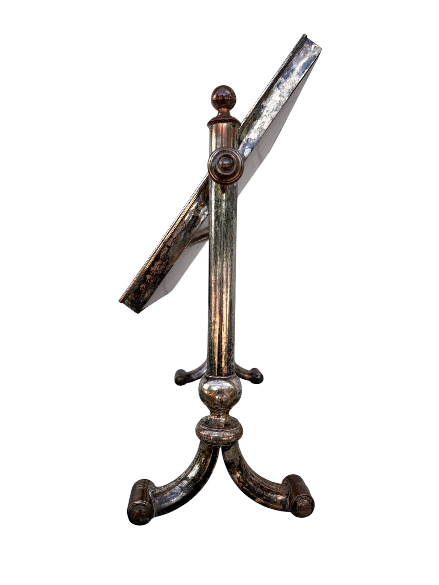 The antique Chevalier Mirror features a rectangular swing frame supported by two turned posts on decorative trestle feet. The mirror stands on four scrolled feet and features its original tarnished, silvered finish. The front of the mirror reflects a bright blue sky with wispy white clouds. The original dark brown backing is still attached to the frame.