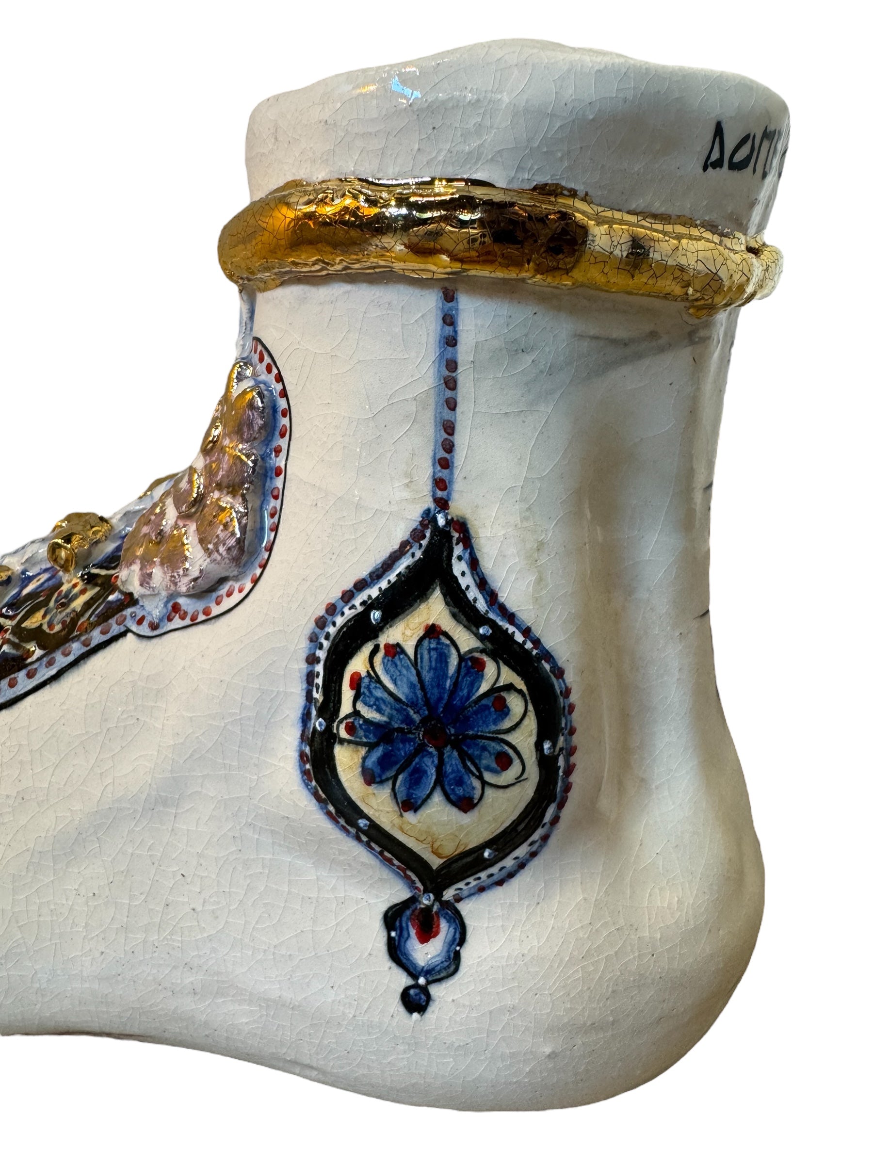 Close-up of a ceramic foot sculpture by Domenico Pinto. The foot is decorated with intricate hand-painted designs inspired by Apulian folklore and accented with 24KT gold. A stylized gilt mask sits atop the foot.