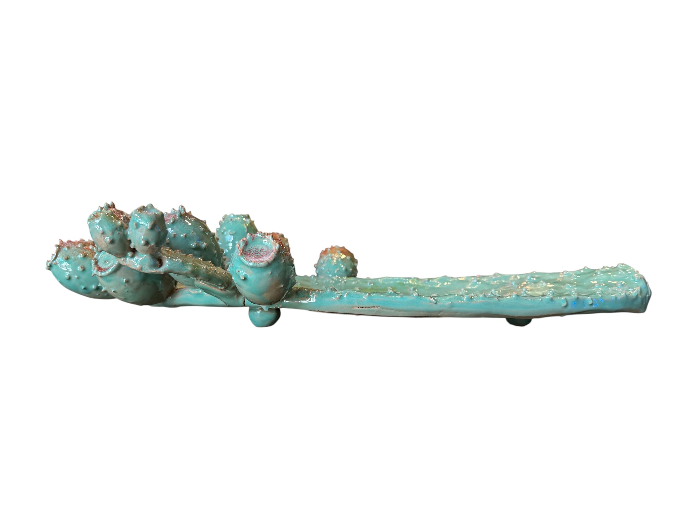 A green and red, glazed ceramic platter in the shape of a prickly pear cactus pad with attached prickly pear fruit. The surface has raised dots representing spines.