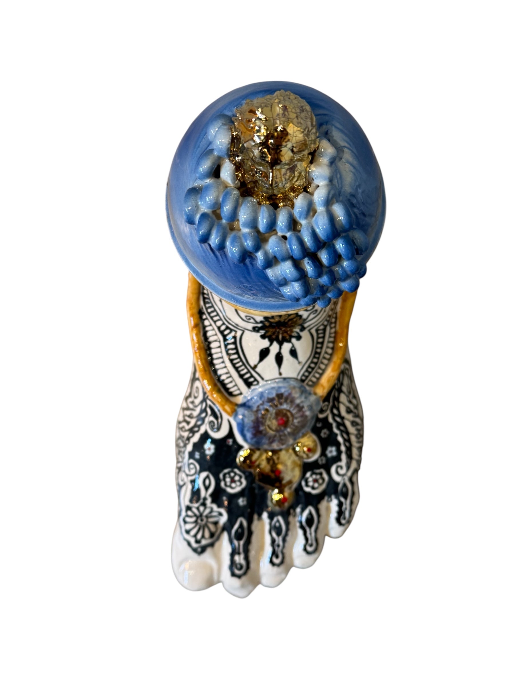 Handcrafted ceramic sculpture in the shape of a foot, decorated with intricate black and white patterns, 24KT gold accents, and topped with a blue lid featuring a gilt fish and head emerging from stylized waves.
