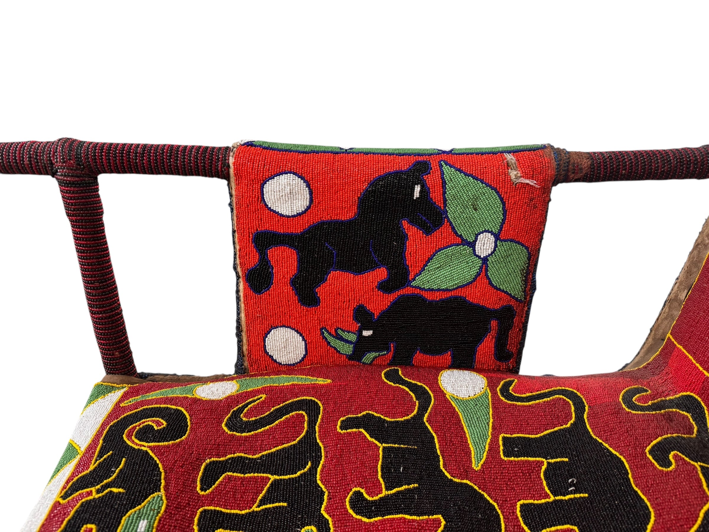 Close-up of a Yoruba beaded armchair, featuring vibrant red, blue, and green beads in a pattern of stylized masks and animals such as lions and zebras