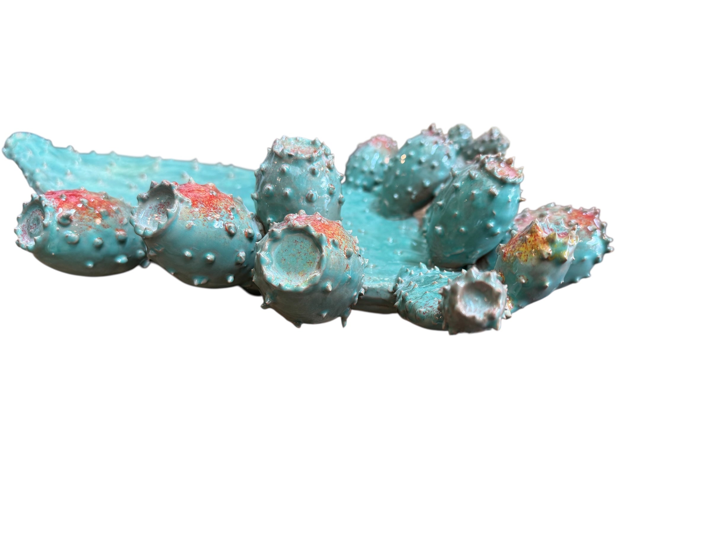 A green and red, glazed ceramic platter in the shape of a prickly pear cactus pad with attached prickly pear fruit. The surface has raised dots representing spines.