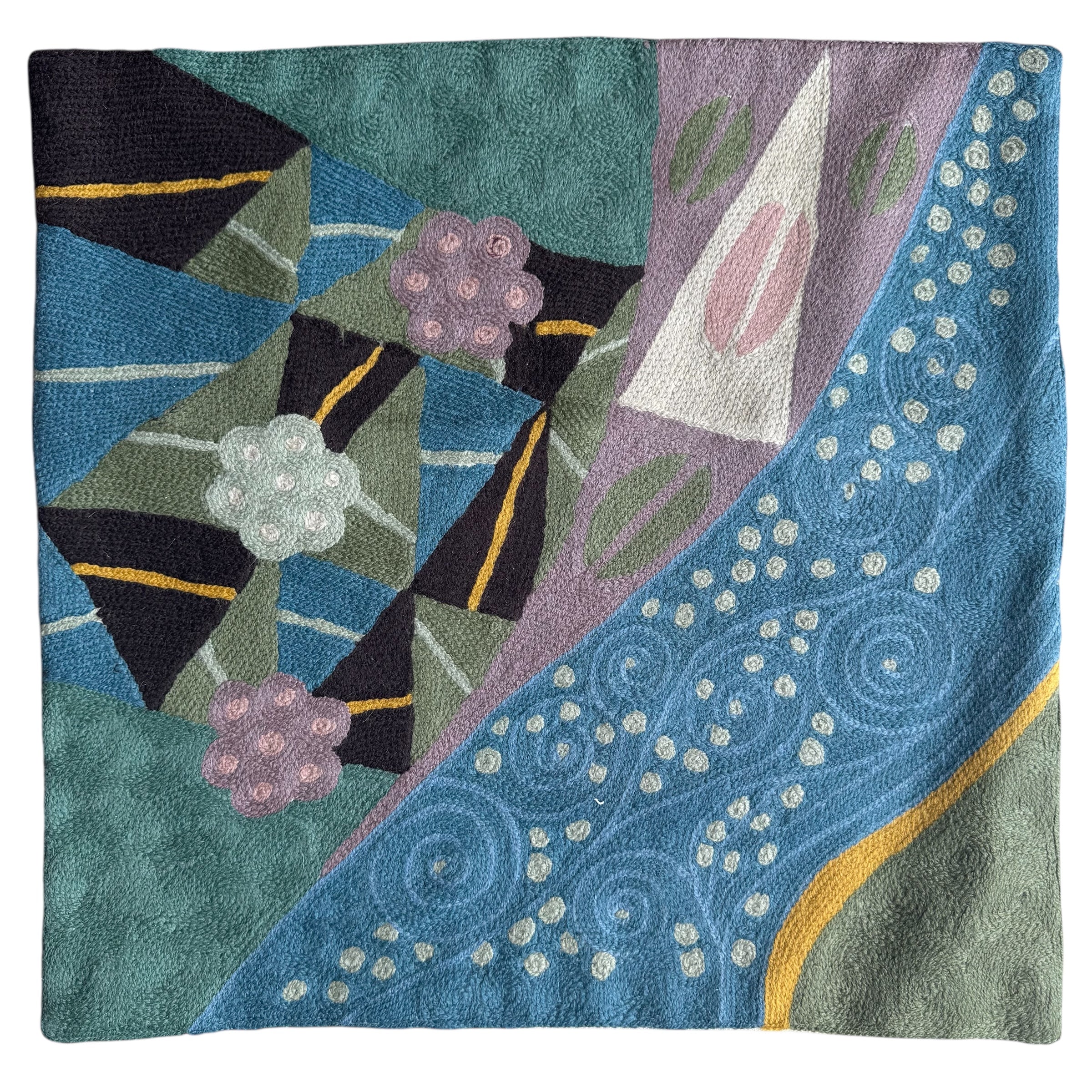 Decorative pillow with geometric patterns and floral elements on a teal background. Vibrant cross-stitched pillows from India with various artistic designs, sourced in Aix-en-Provence.
