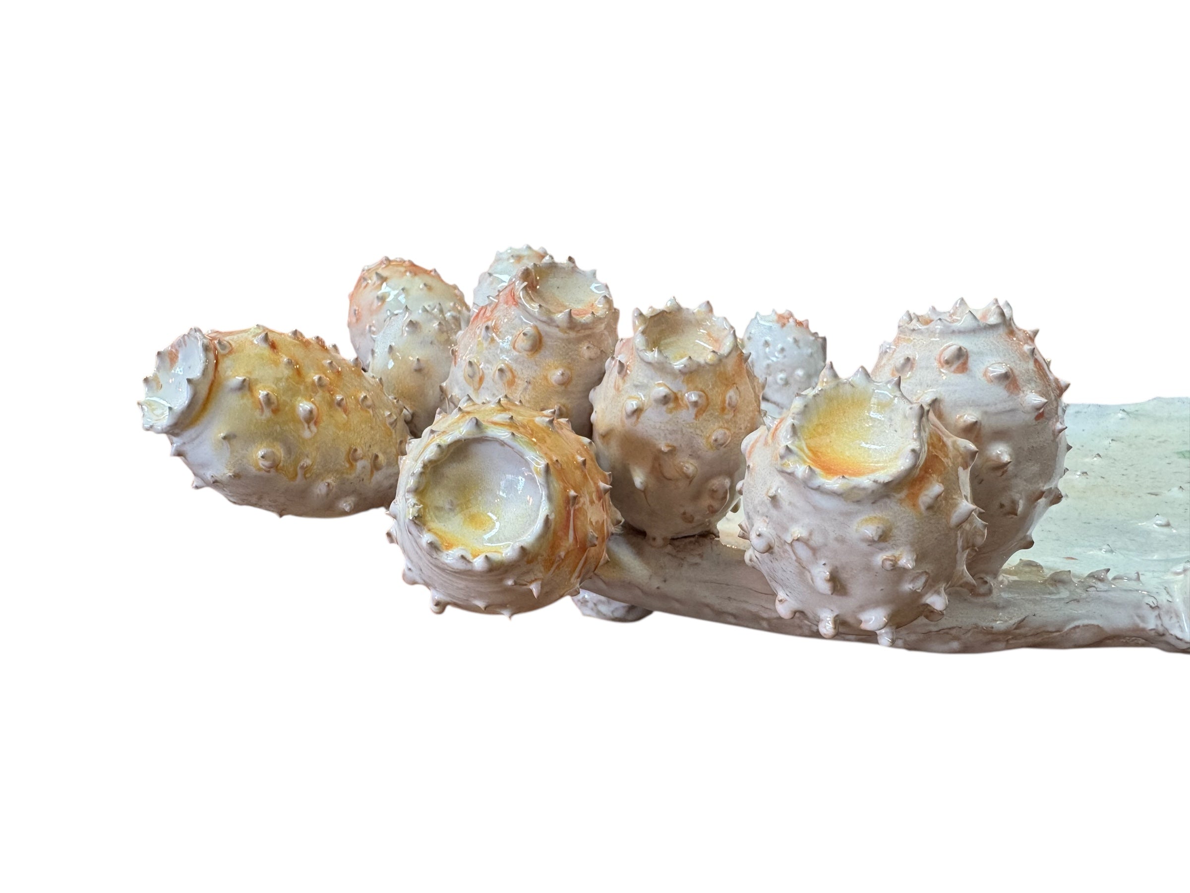 A white and orange, glazed ceramic platter in the shape of a prickly pear cactus pad with attached prickly pear fruit. The surface has raised dots representing spines.
