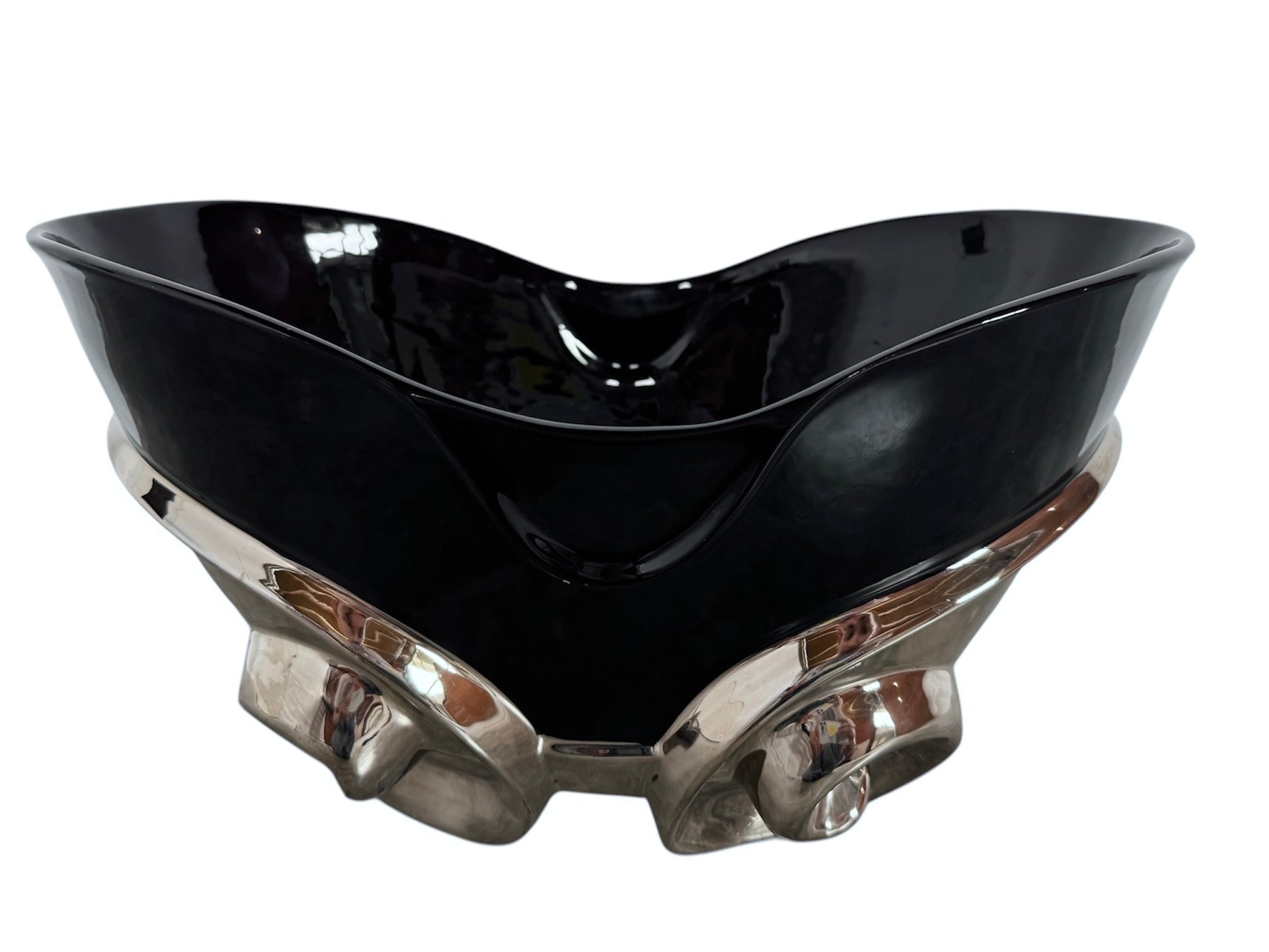 A large, decorative ceramic bowl by Dolbi Cashier in a dramatic Postmodern style. The top half is finished in a polished, piano-black glaze with an organic, wavy "butterfly" rim that dips in the center and rises at the sides. The bottom half is finished in a reflective, metallic silver chrome glaze, featuring bold, geometric-rounded feet and a structured base that appears to "hold" the black vessel. The overall shape is wide and sculptural, reminiscent of 1980s Art Deco Revival.