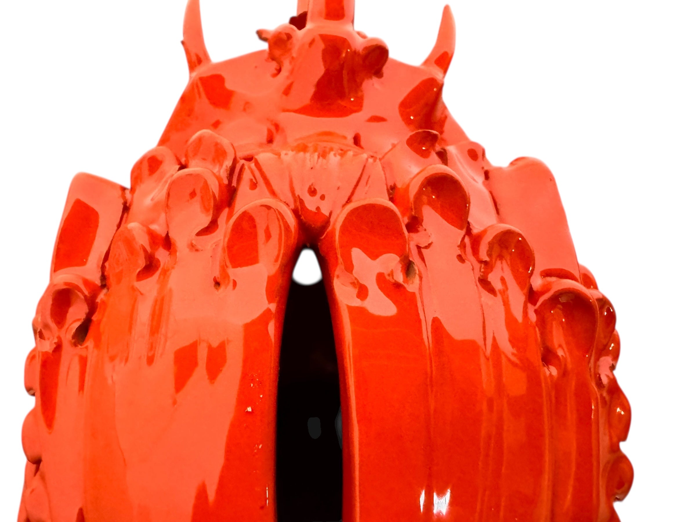 A glossy, vibrant orange ceramic sculpture of a rhinoceros beetle by Enza Fasano. The piece features a highly polished, reflective glaze and stylized, fluid anatomical details. Its prominent dual horns curve forward, and the body is textured with layered, wing-like plates, set against a plain white background.