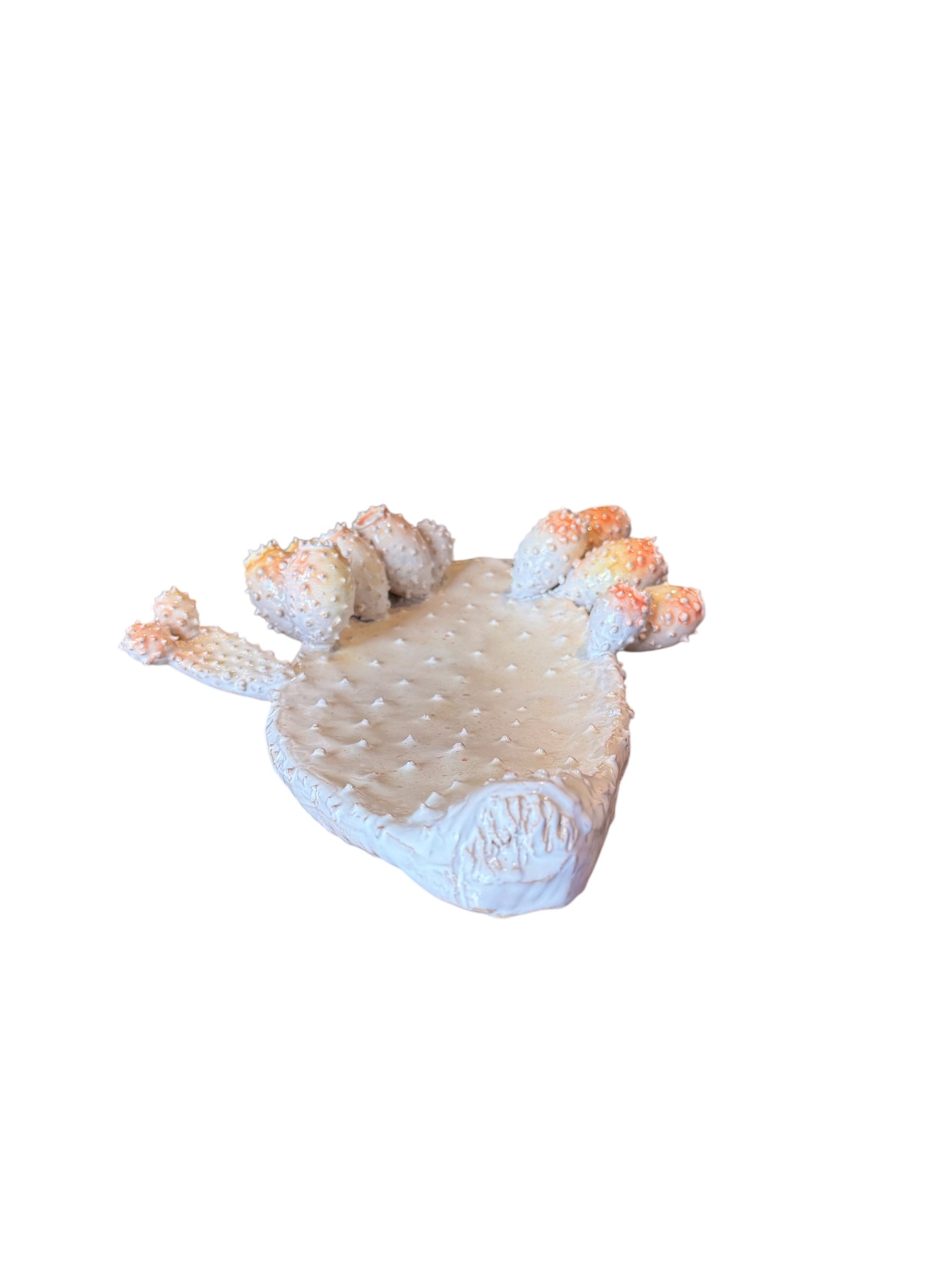 A white and orange, glazed ceramic platter in the shape of a prickly pear cactus pad with attached prickly pear fruit. The surface has raised dots representing spines.