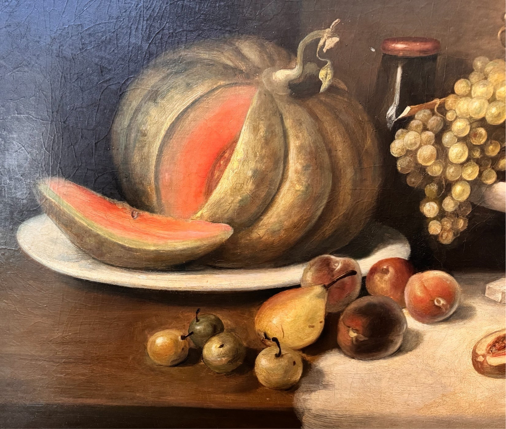 Oil painting, 'Still Life with Fruit and Cheese' by Michel Rivol, 1887. Features grapes, melons, cheese under a glass dome, and a bottle on a tablecloth against a dark background