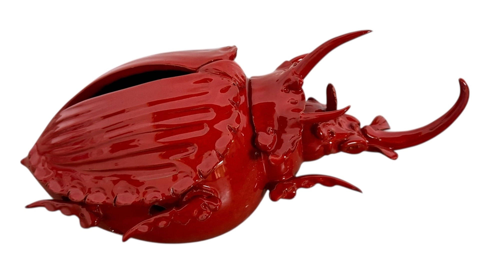 A vibrant, glossy red ceramic sculpture of a rhinoceros beetle by Enza Fasano. The piece features a highly reflective, deep crimson glaze that accentuates its smooth, rounded abdomen and the intricate, jagged textures of its head and horns.