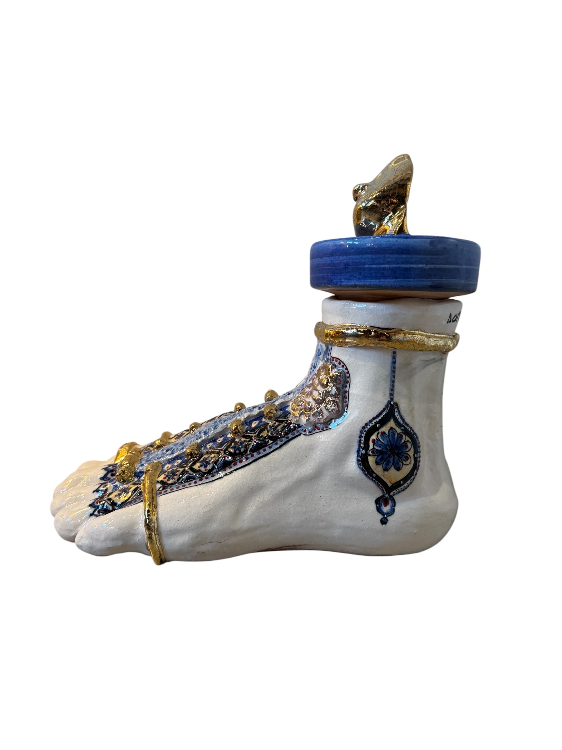 Close-up of a ceramic foot sculpture by Domenico Pinto. The foot is decorated with intricate hand-painted designs inspired by Apulian folklore and accented with 24KT gold. A stylized gilt mask sits atop the foot.