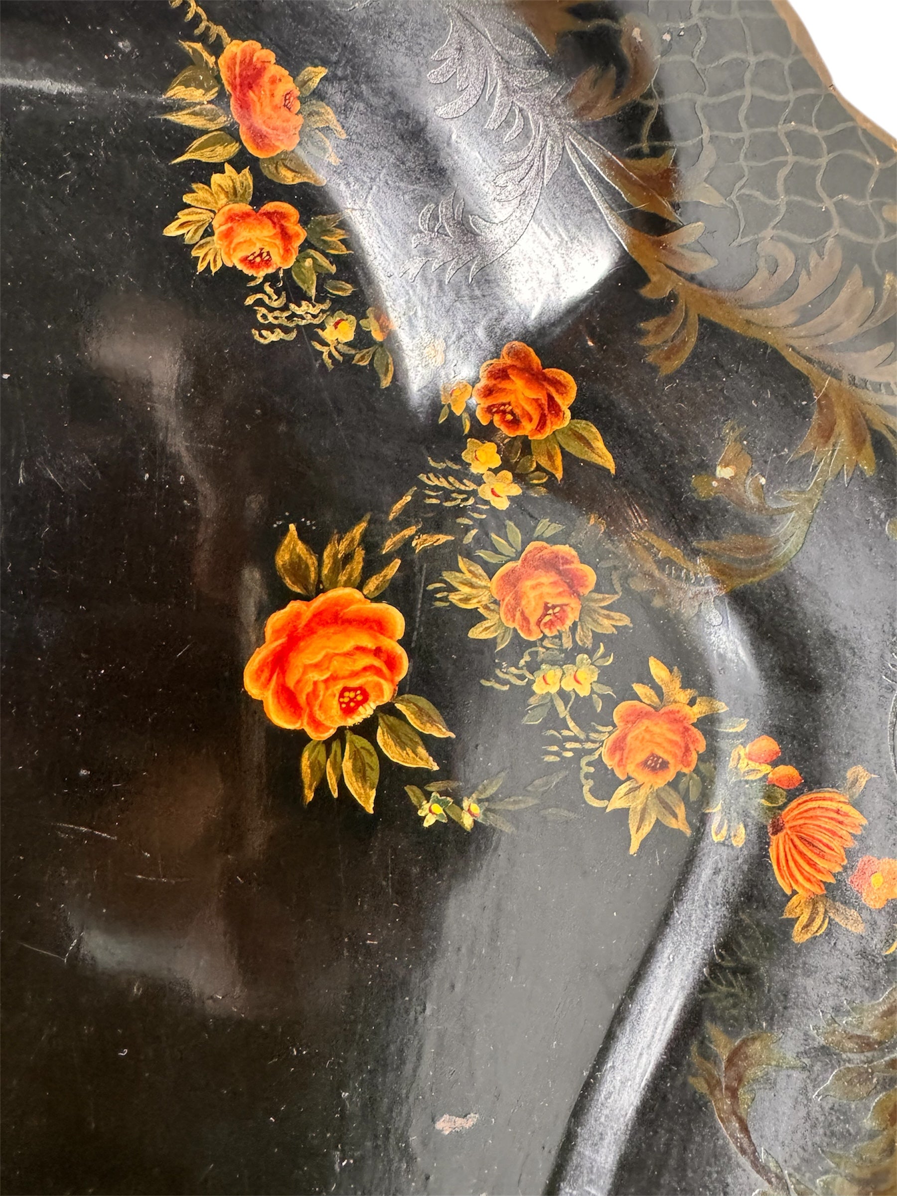 A vintage rectangular toleware serving tray with a scalloped, wavy edge and a black lacquered finish. The tray features hand-painted floral motifs in a traditional folk-art style. At the bottom center is a large, vibrant cluster of yellow and orange roses and daisies with green leaves. Smaller floral sprays and delicate gold filigree scrollwork decorate the corners and the upper rim. The center of the tray is open black space, showing light surface wear and minor scuffing consistent with age.
