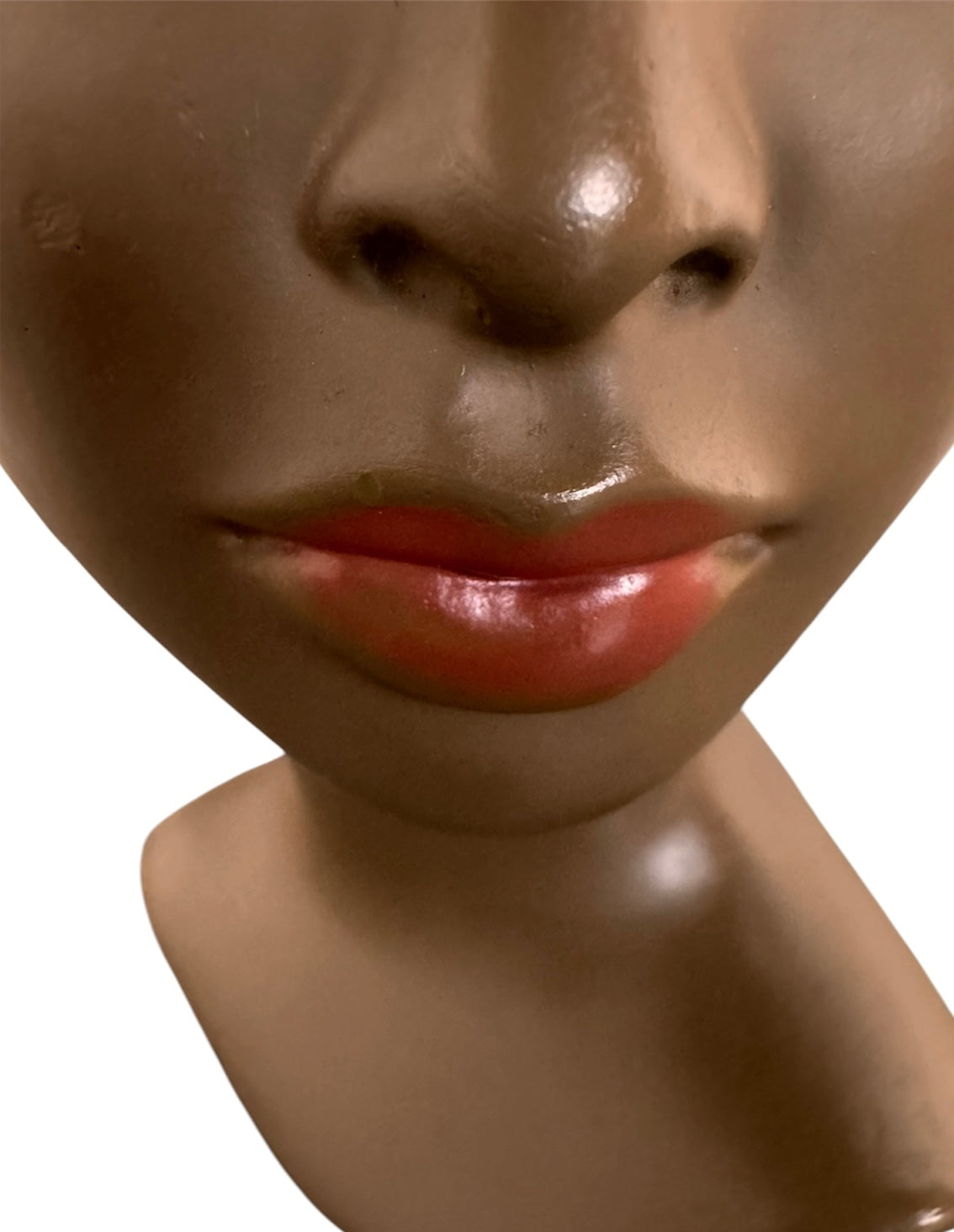 a vintage ceramic bust featuring a woman with brown skin, dark eyes, and orange lips. Her black hair is sleek and parted on the side, pulled back into a low style. She wears a small, round white earring in her right ear lobe. The bust includes her head, neck, and the upper part of her shoulders
