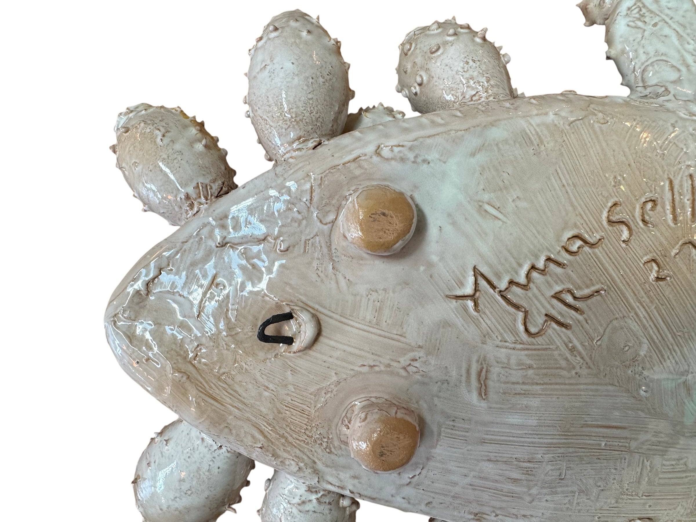 A white and orange, glazed ceramic platter in the shape of a prickly pear cactus pad with attached prickly pear fruit. The surface has raised dots representing spines.