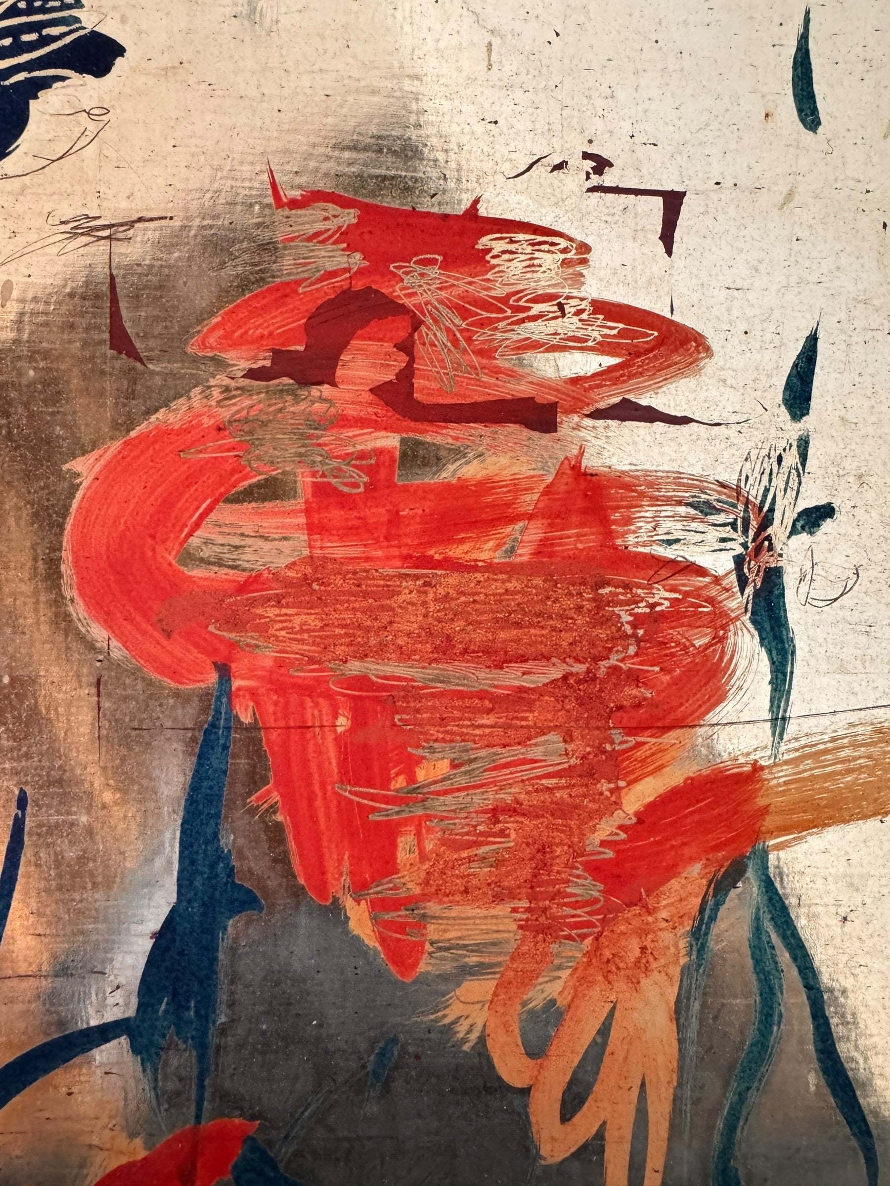 A vertical composition on a bright, reflective metallic background (likely silver or light gold leaf). The piece is defined by sparse, high-energy gestures: a sweeping arc of orange and red at the top, a central cluster of textured red paint, and a scattering of teal-blue "C" shapes and hooks. The metallic surface is highly visible, giving the piece a luminous, modern feel.