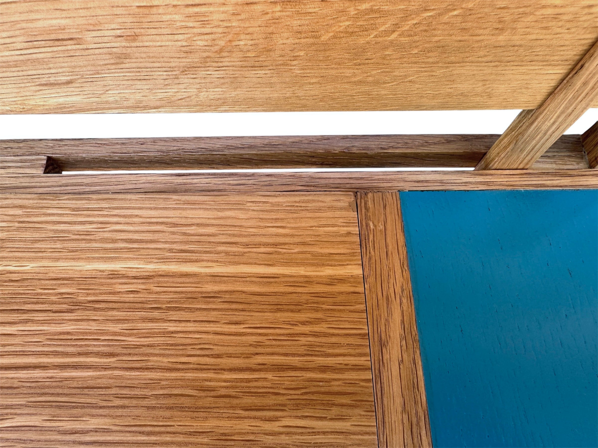 A three-tiered wooden shelving unit featuring a mix of light oak and teal-colored panels. The piece has an open, structural design with visible joinery, vertical supports that extend past the top shelf, and a horizontal backrest at the top. The middle and bottom shelves feature slatted wood center sections flanked by solid teal panels, while the top surface is primarily solid wood with teal accents at the edges.
