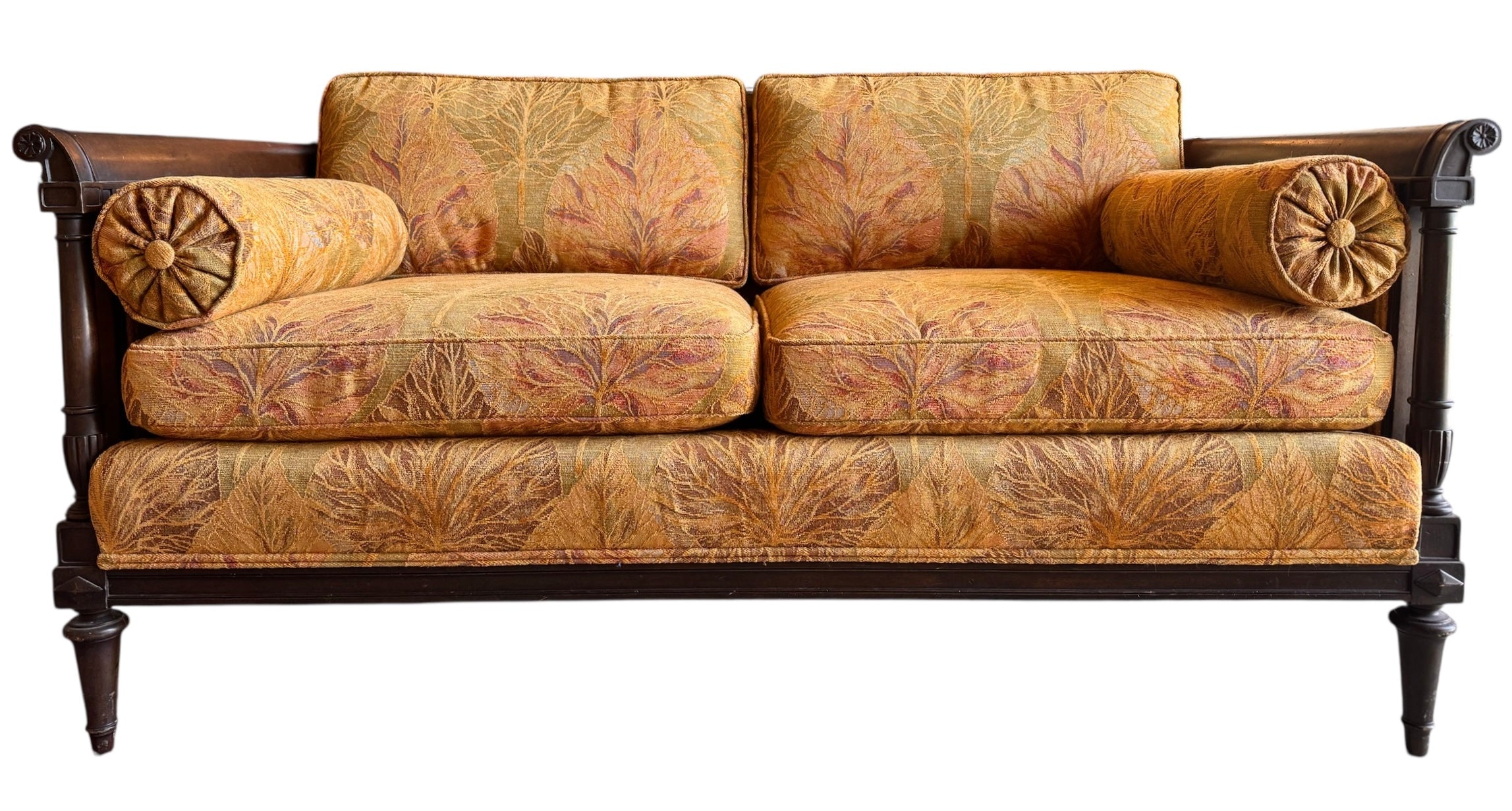 An elegant, two-seater Neoclassical-style settee featuring a dark wood frame and golden-orange botanical upholstery. The settee has a straight back with two rectangular cushions and two matching bolster pillows tucked against the scrolled, dark wood arms. The fabric is a rich tapestry weave with a large-scale, stylized leaf pattern in autumnal shades of gold, amber, and terracotta. The wooden frame is detailed with fluted stiles and tapered, turned legs.