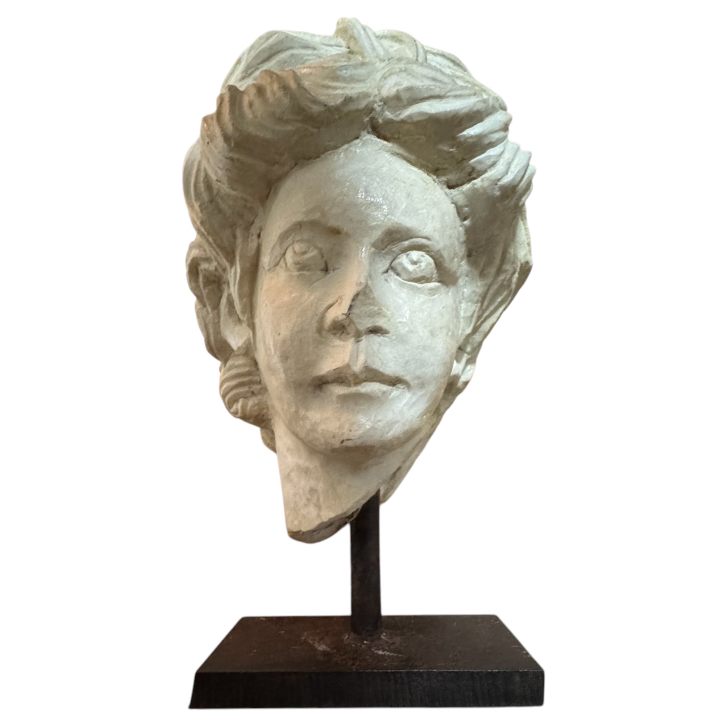 Marble bust of a Roman-style face with coiffure, displayed on an iron stand.