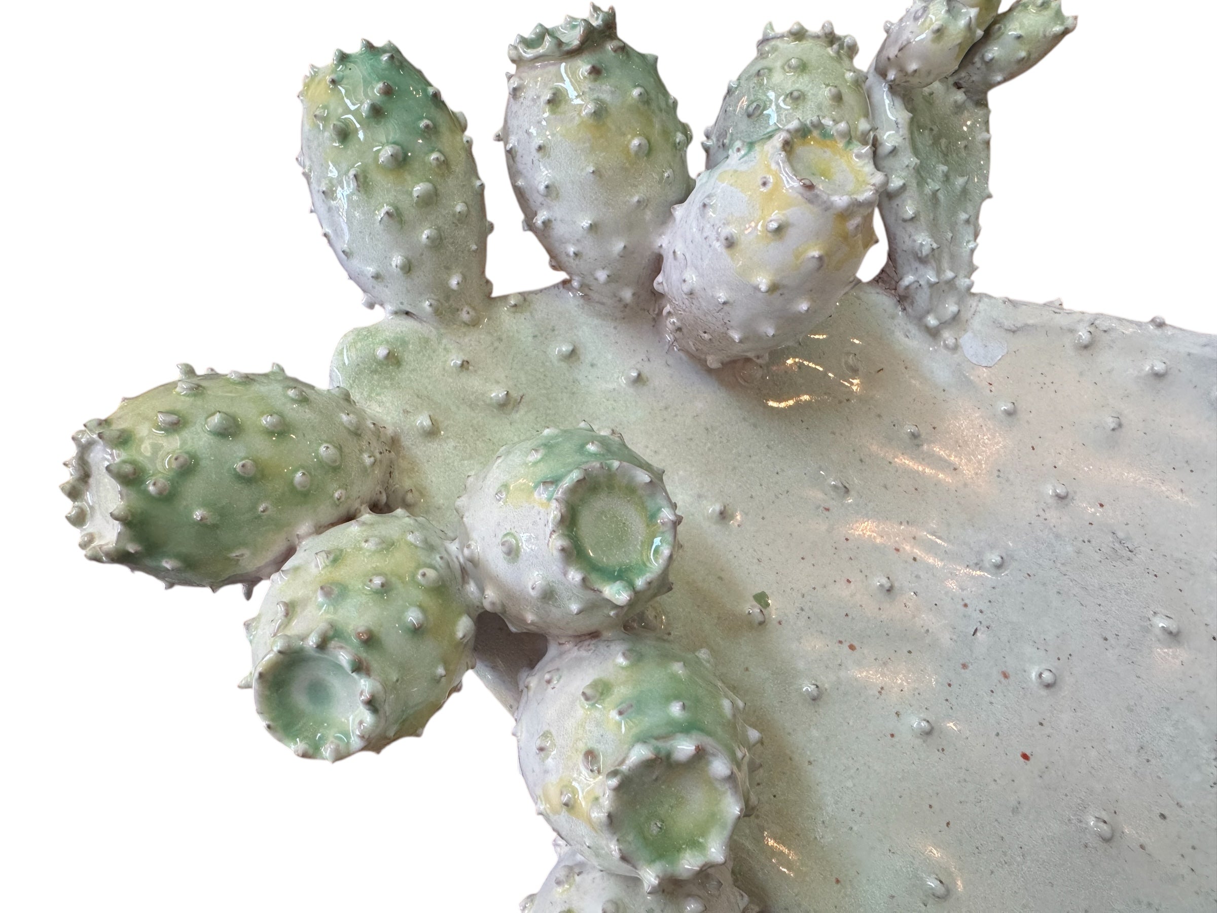 A white and green, glazed ceramic platter in the shape of a prickly pear cactus pad with attached prickly pear fruit. The surface has raised dots representing spines.
