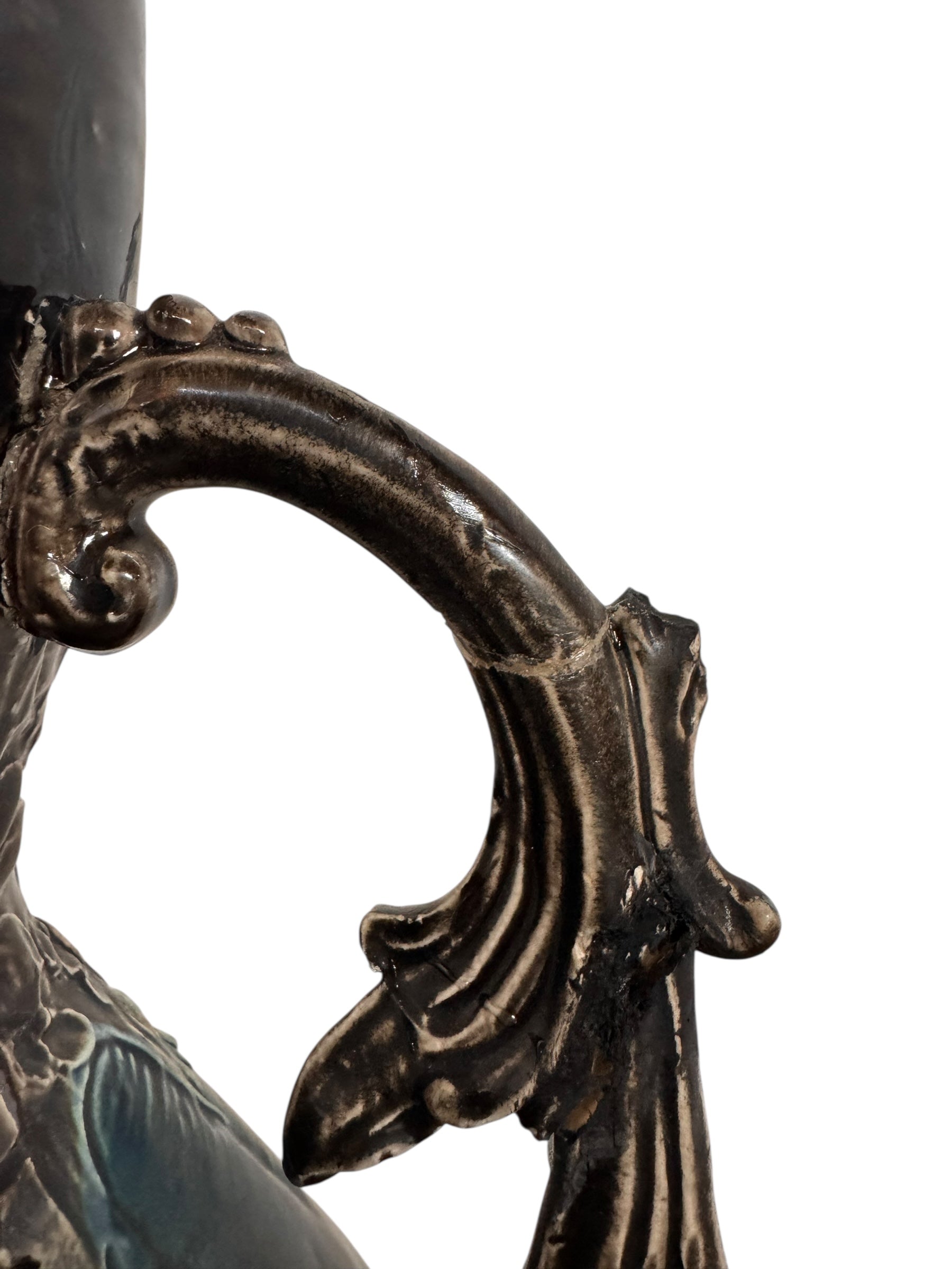 An ornate, dark glazed ceramic Art Nouveau vase with two handles and raised floral designs in yellow, purple, and green.