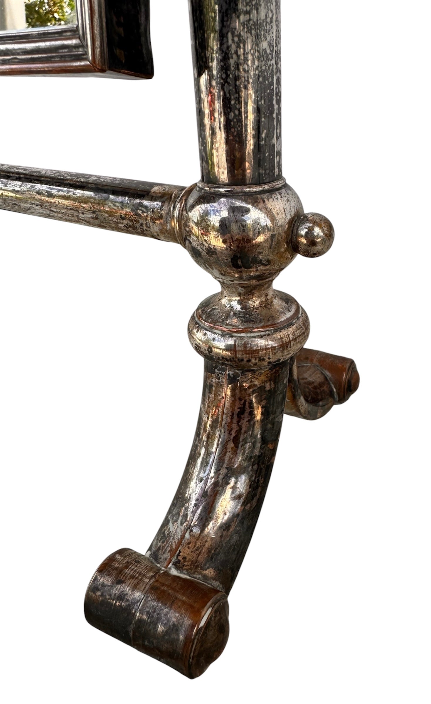 The antique Chevalier Mirror features a rectangular swing frame supported by two turned posts on decorative trestle feet. The mirror stands on four scrolled feet and features its original tarnished, silvered finish. The front of the mirror reflects a bright blue sky with wispy white clouds. The original dark brown backing is still attached to the frame.